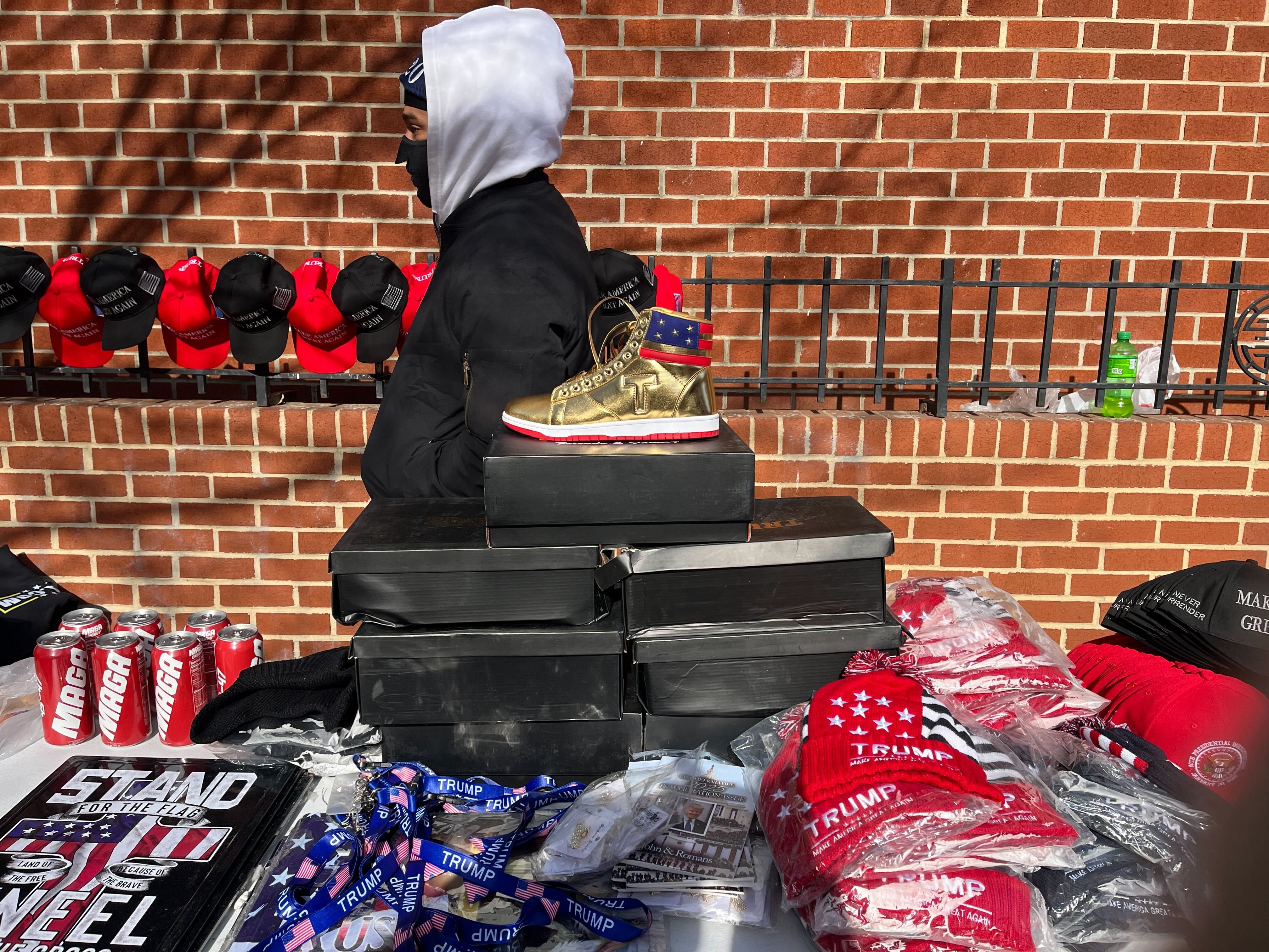 A golden hightop sneaker atop black shoe boxes on a table of merchandise for Trump.