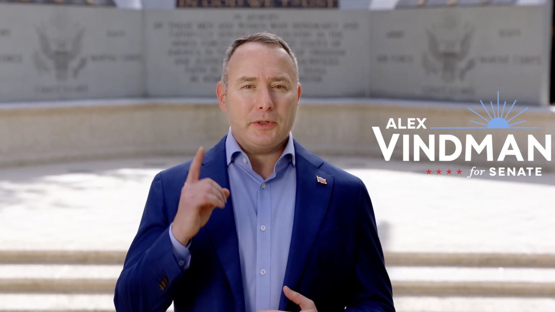 Man in blue suit and light blue shirt standing outdoors, gesturing with one finger raised, with text "Alex Vindman for Senate" beside him.