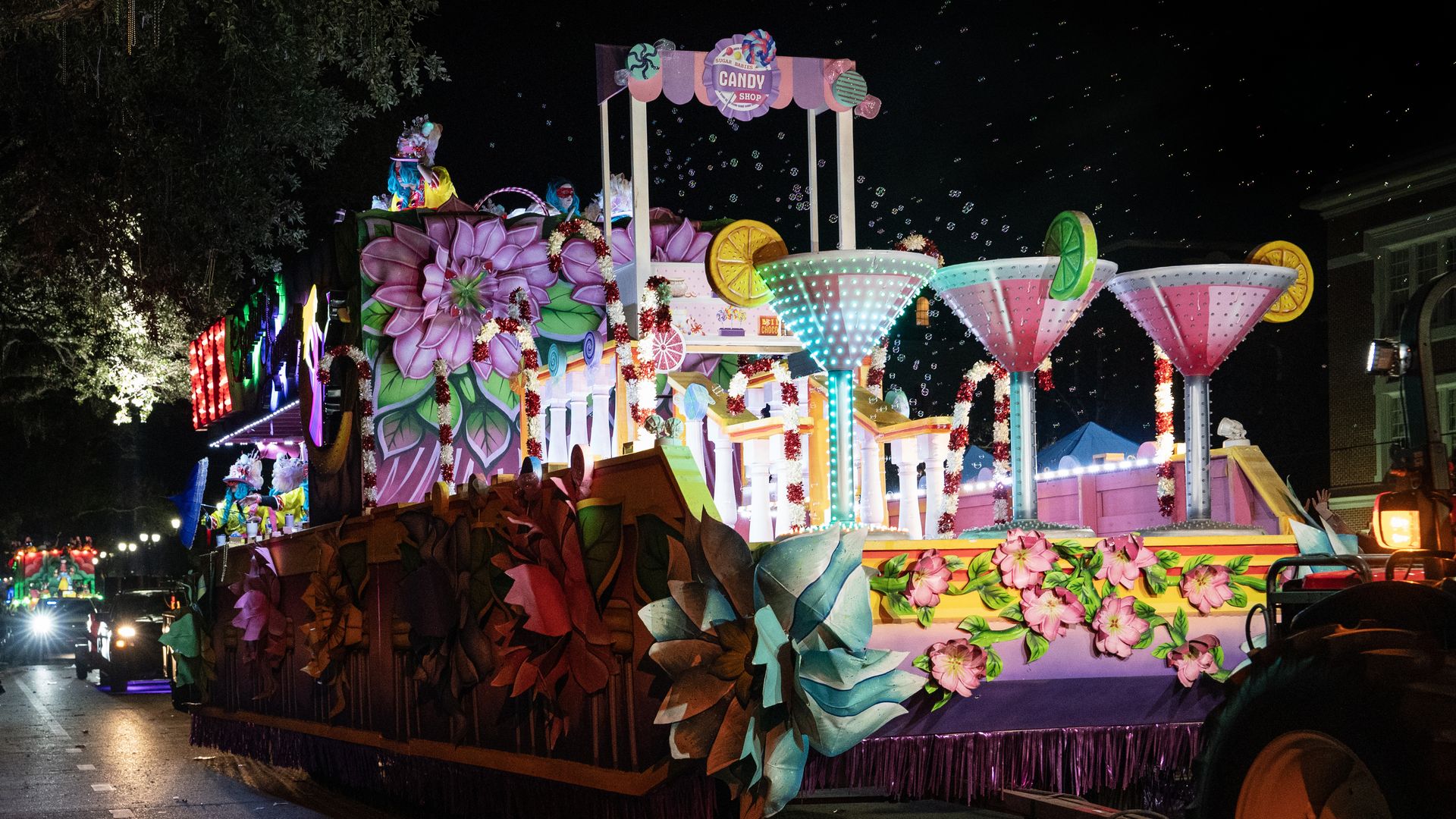 A Mardi Gras float rolls down the parade route. The float shows three larger-than-life martinis at the front.