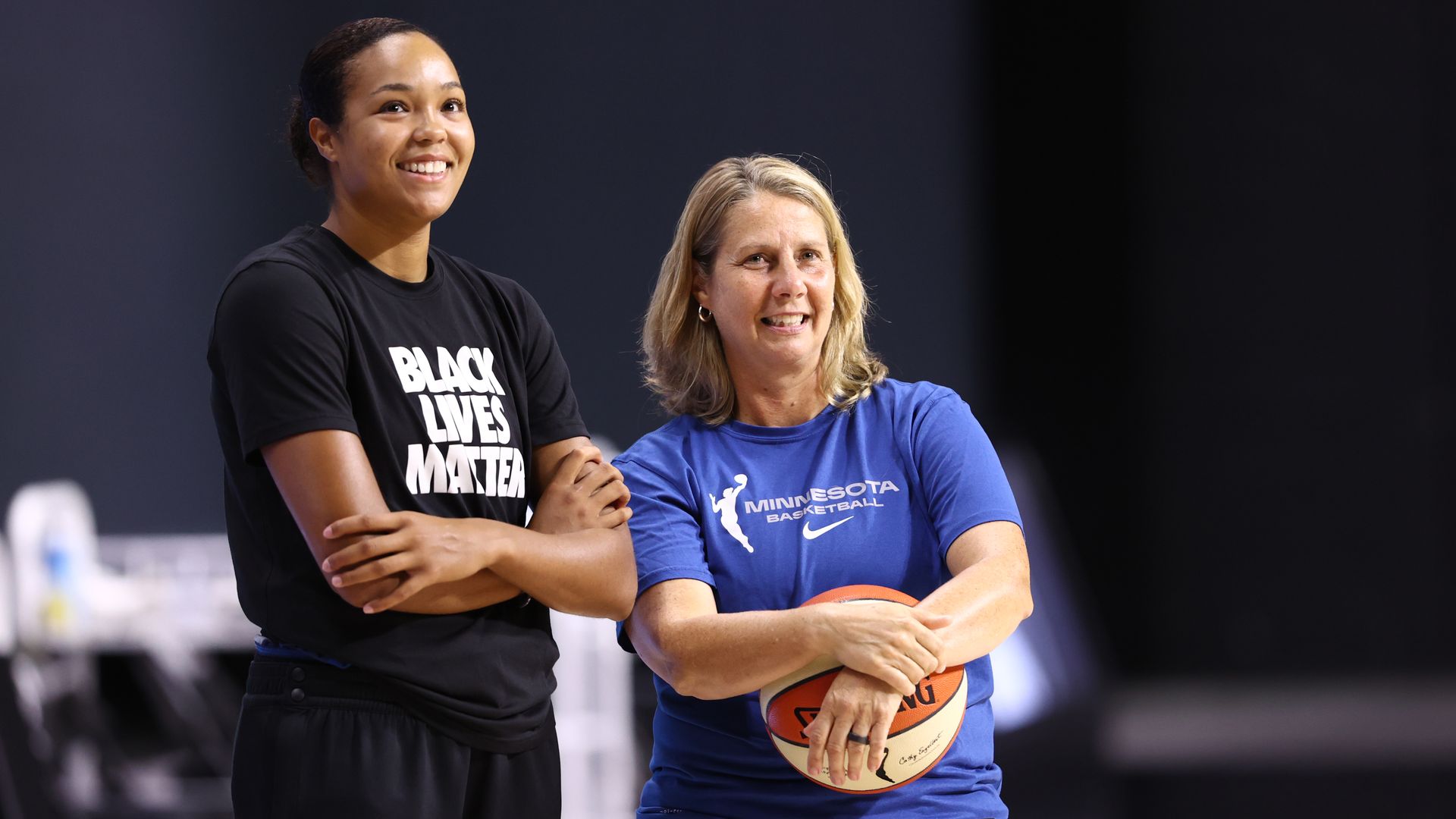 Cheryl Reeve wears a blue shirt and holds a basketball next to Napheesa Collier 