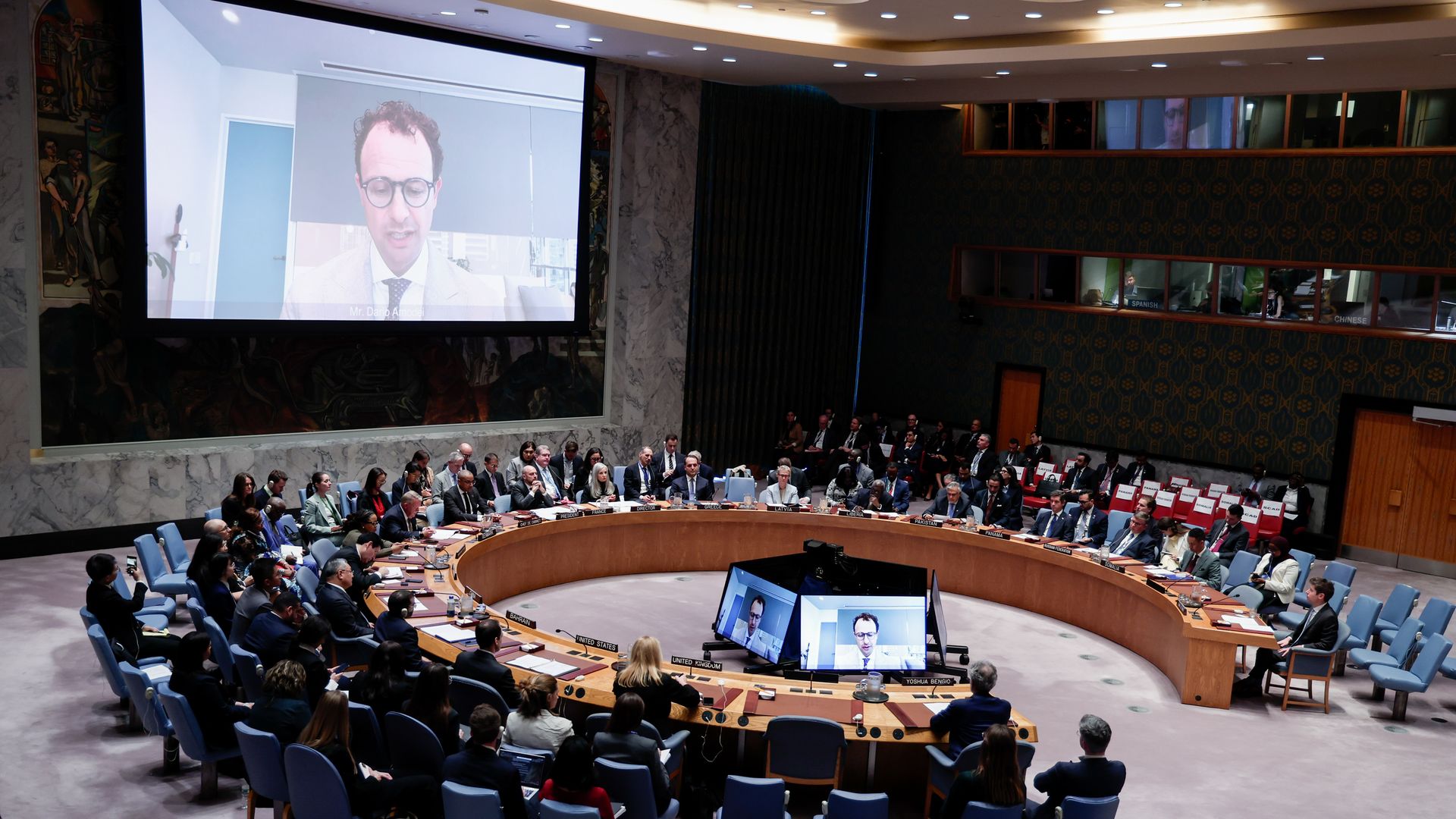 Dario Amodei seen on a large screen over a horseshoe table surrounded by diplomats.