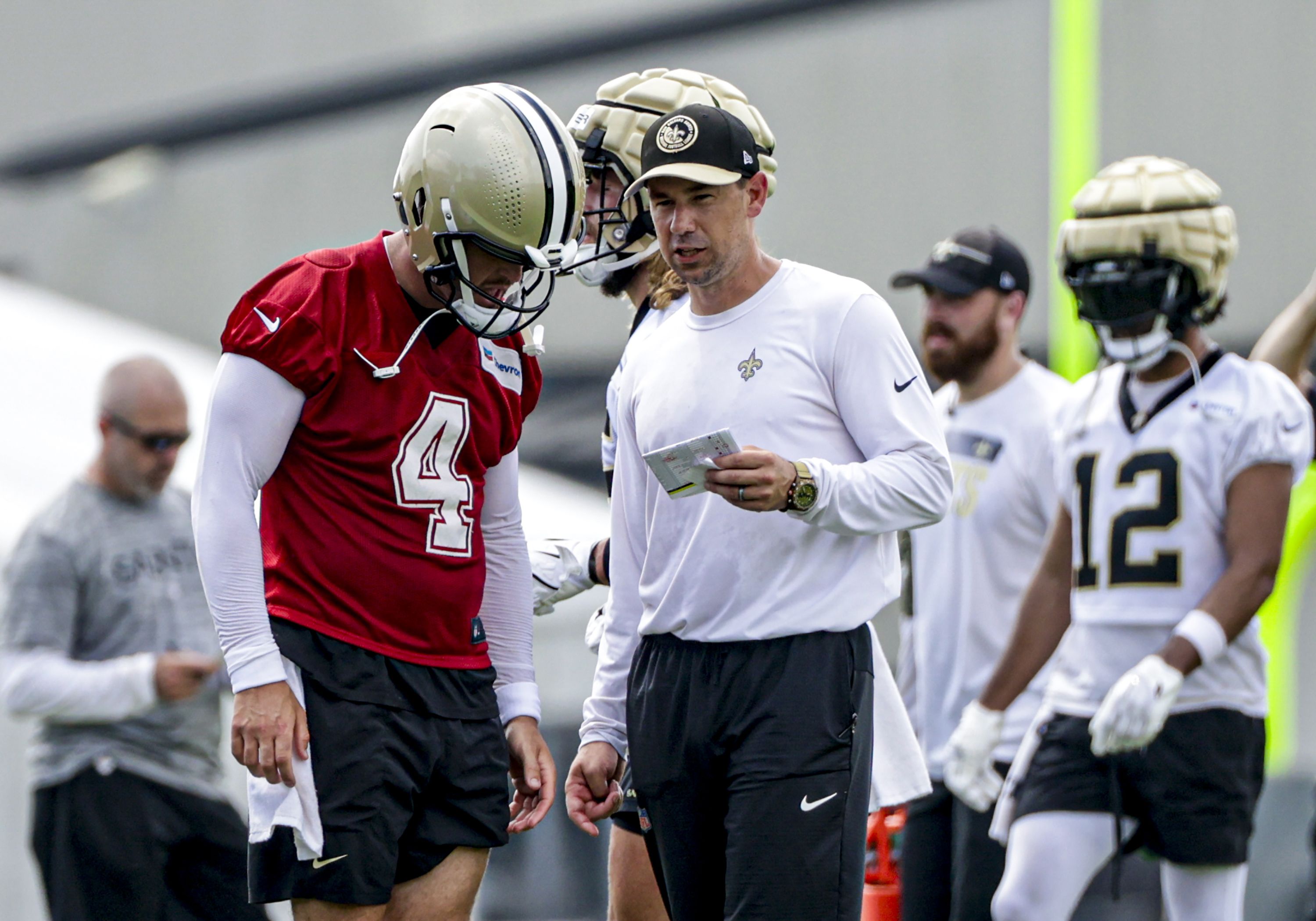 A football player wearing a red jersey leans his head in to talk to a coach, who holds up a piece of paper as they speak.