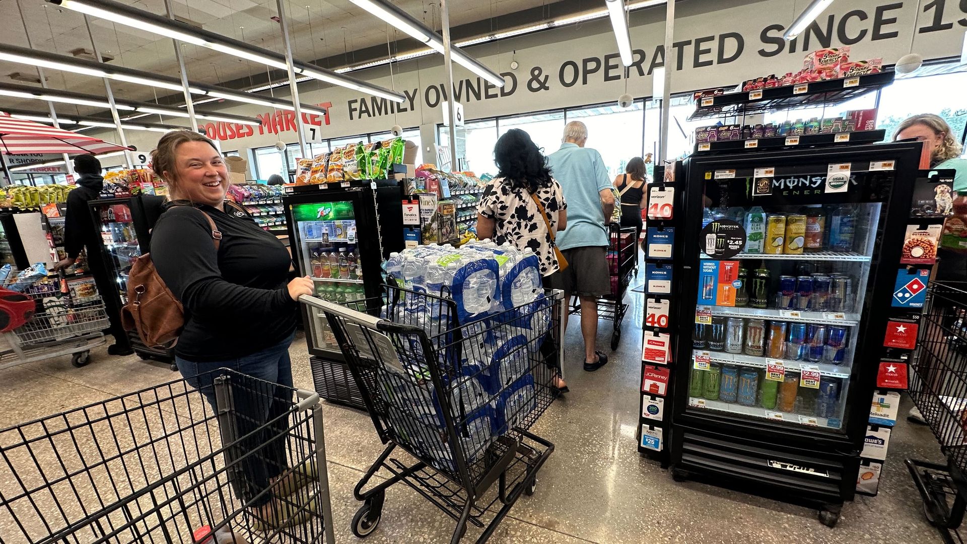 A woman stands in line at a grocery store with her grocery cart full of bottled water.