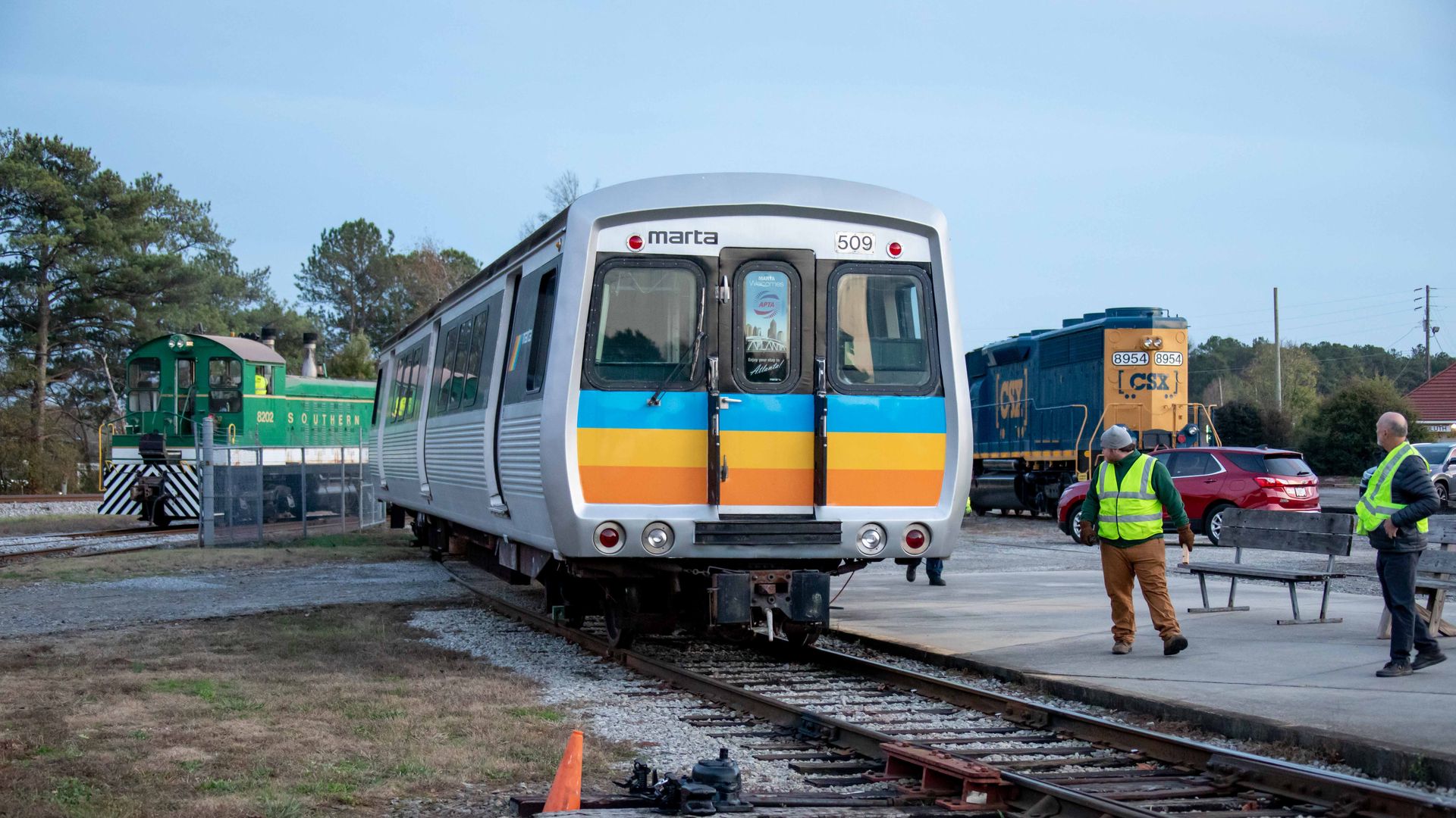 A MARTA rail car with orange, yellow and blue stripes rides on a track at a museum about trains