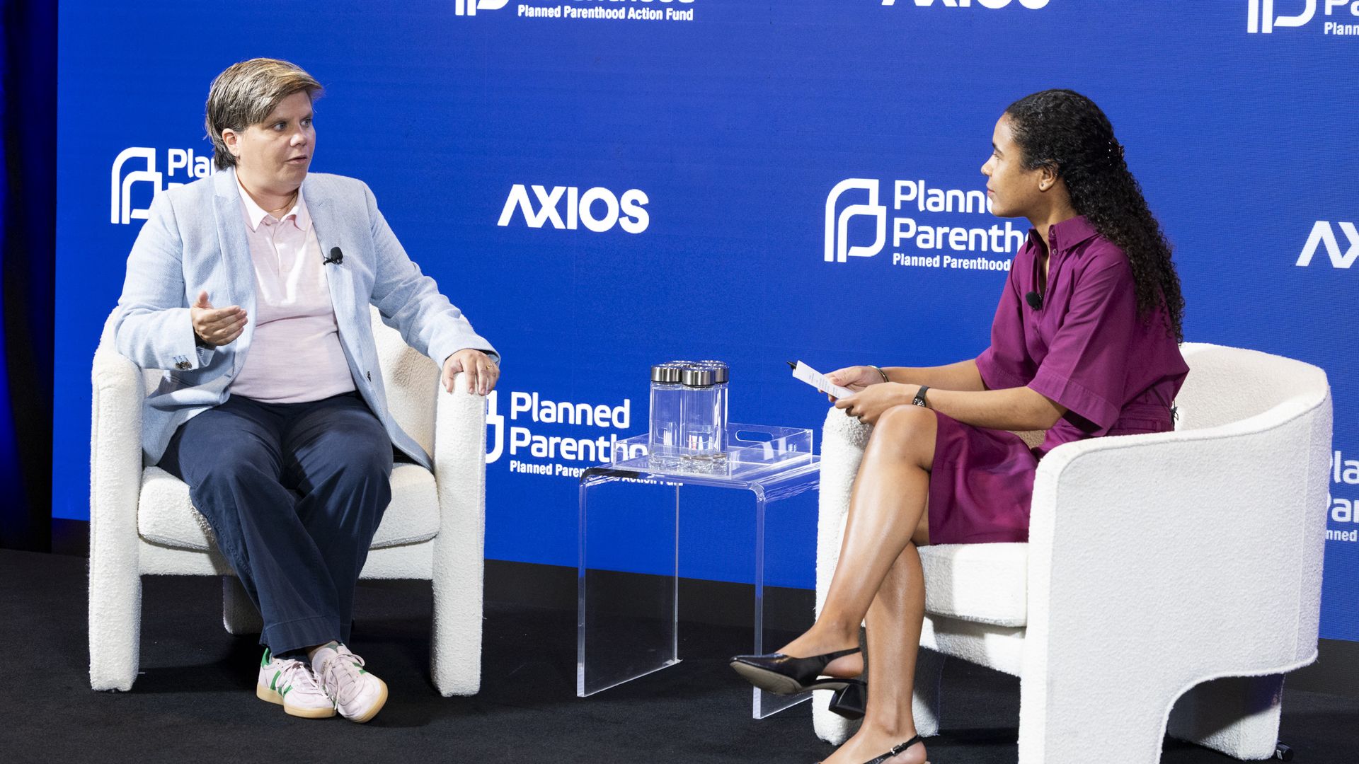 Two people sit on stage in chairs against a blue backdrop with Axios and Planned Parenthood logos. A man in a light blue blazer speaks; a woman in a purple dress listens, holding notes.