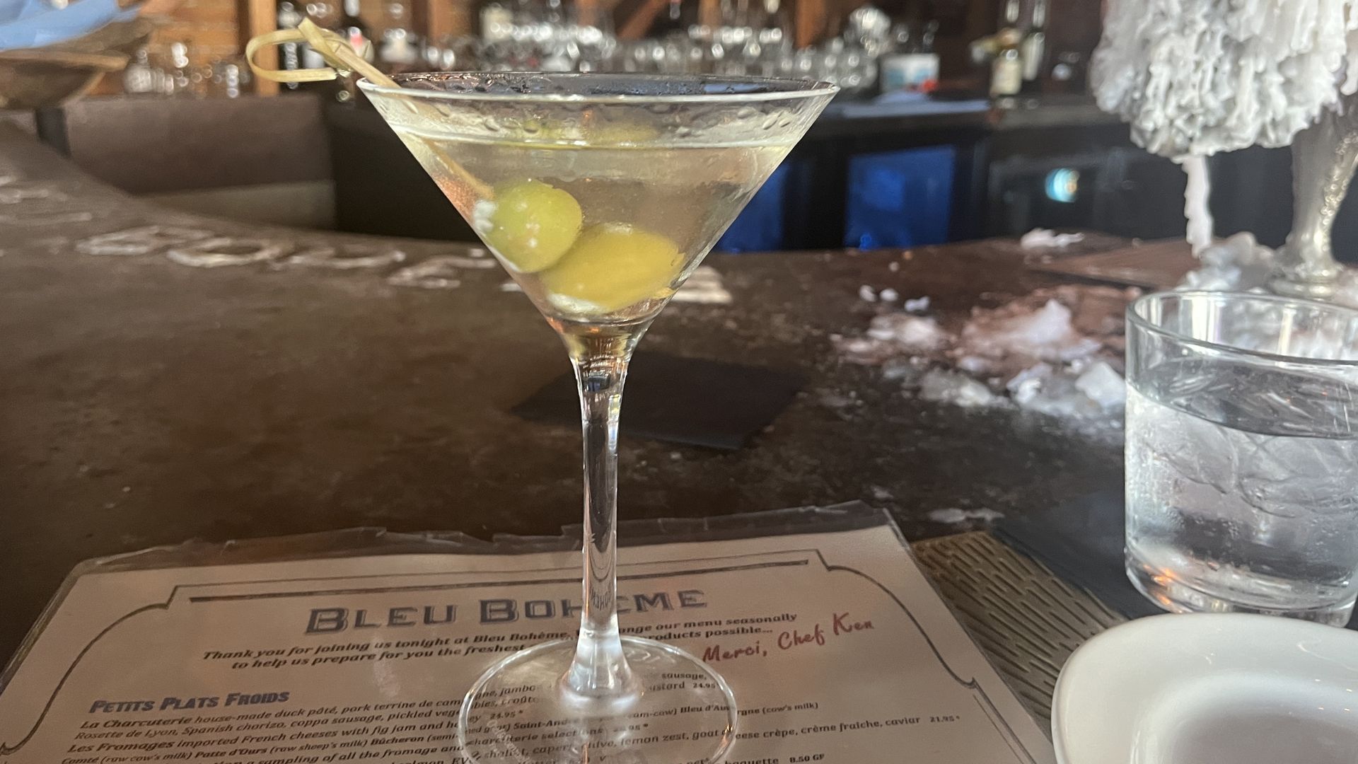 A Martini on top of a Bleu Boheme menu on top of its stone bar