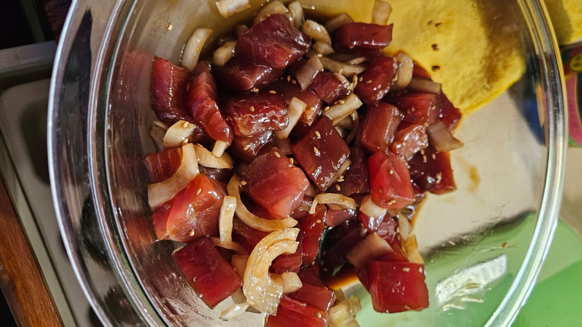 Glass bowl containing chunks of marinated raw tuna with sliced onions and sesame seeds.