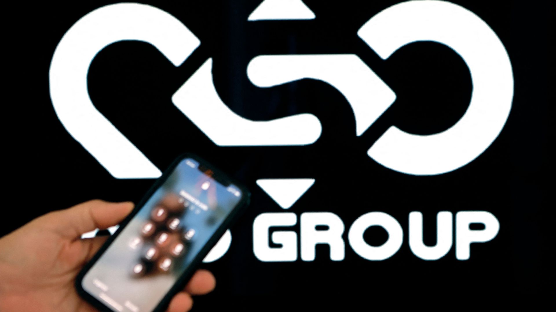 A photo illustration of a smartphone in front of the NSO Group logo