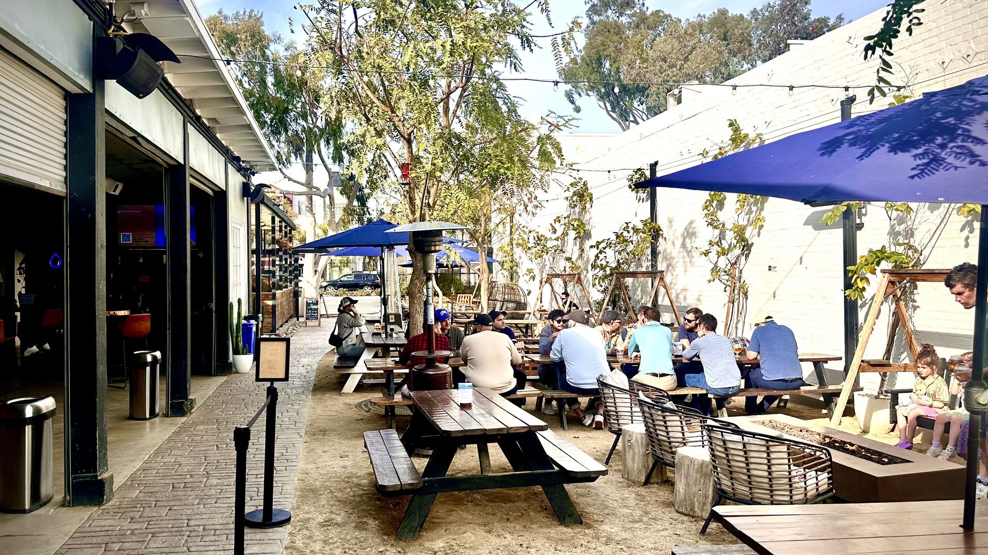 an outdoor beer garden with picnic tables and umbrellas next to garage door entry to a bar area