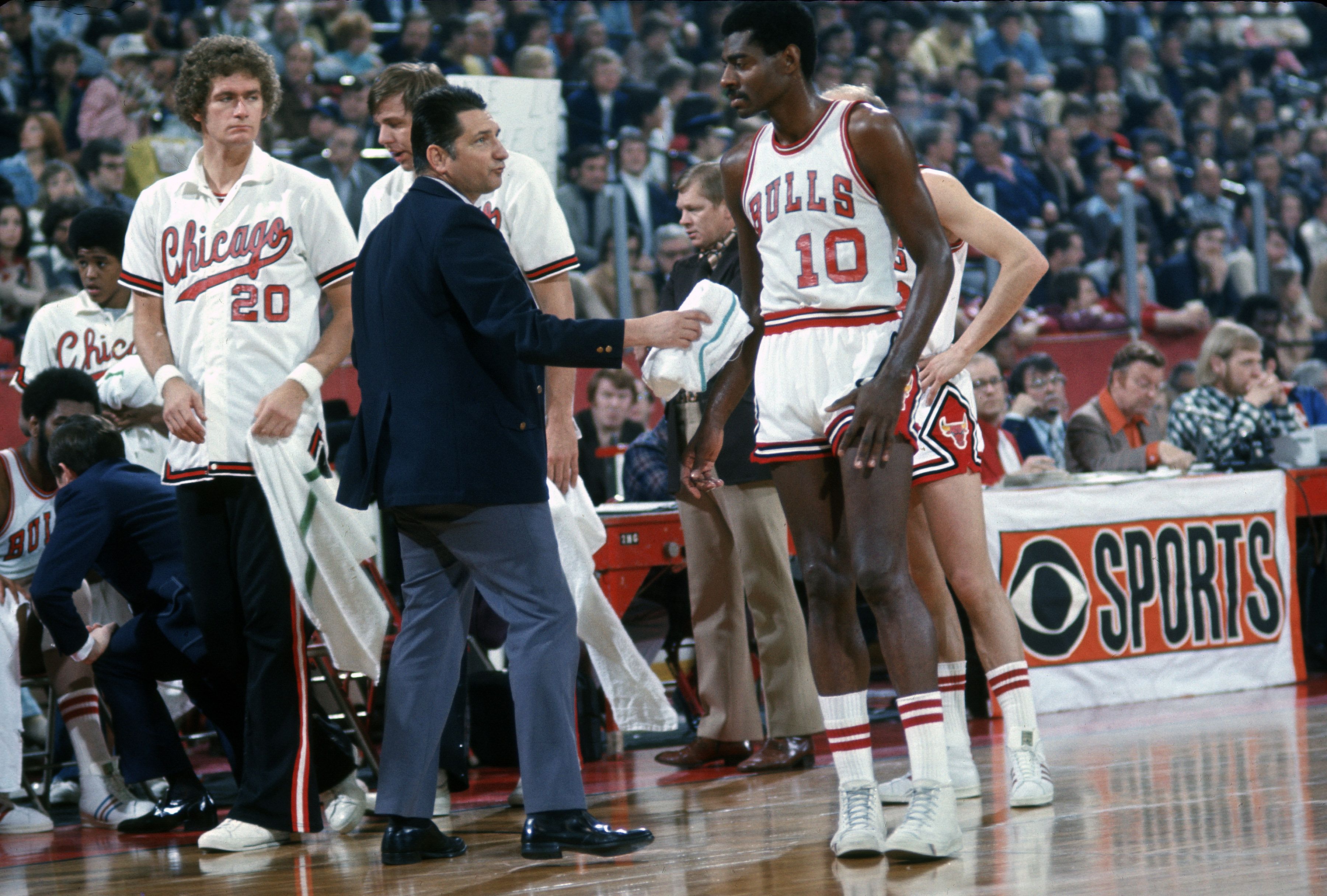 Photo of a basketball player in a uniform grabbing a towel after sweating on a basketball court. 