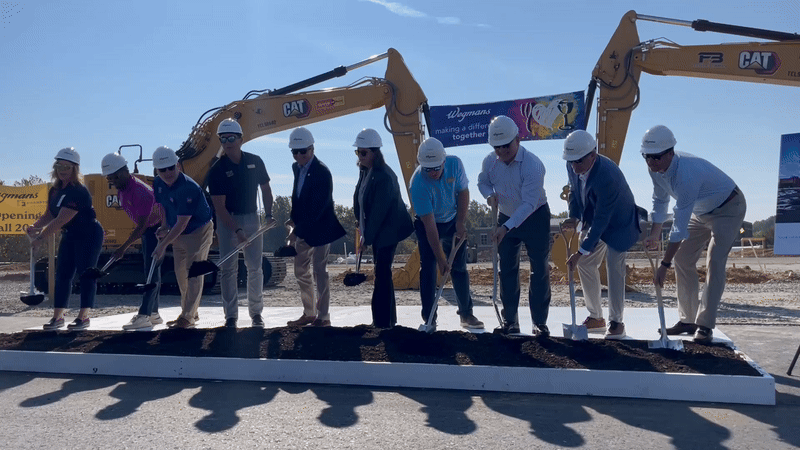 A GIF of people wearing hard hats at a groundbreaking, moving dirt with shovels