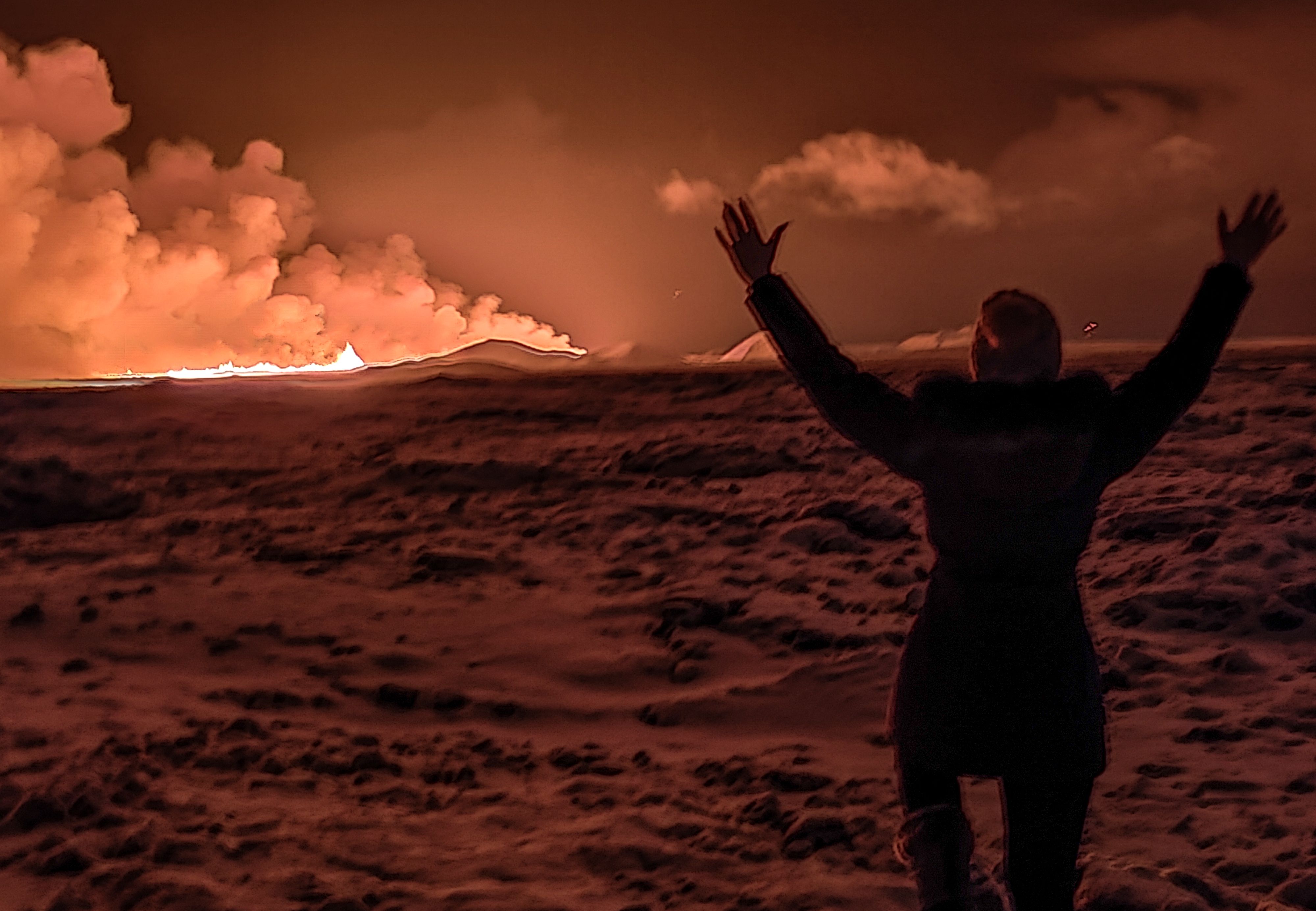 A local resident watch smoke billow as the lava colour the night sky orange from an volcanic eruption on the Reykjanes peninsula 3 km north of Grindavik, western Iceland on December 18.