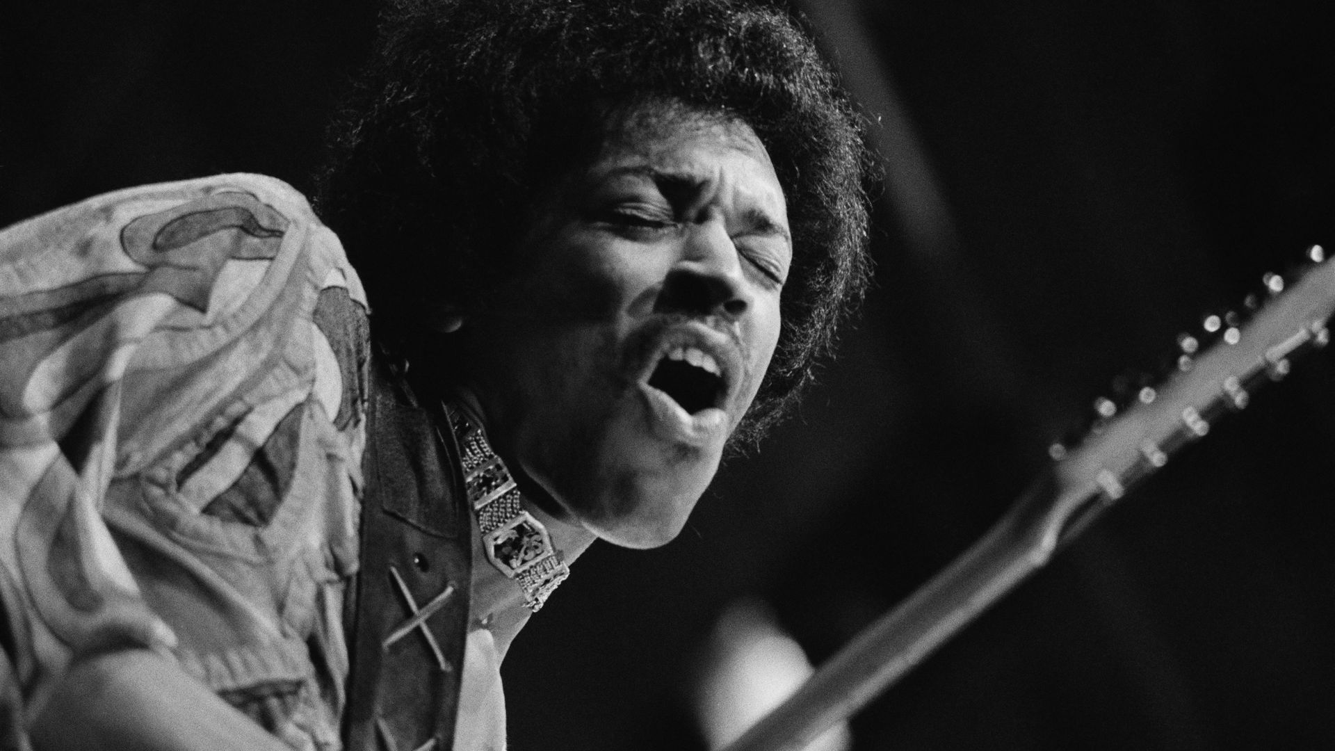 A black and white photo of Jimi Hendrix singing while playing guitar. His eyes are closed.
