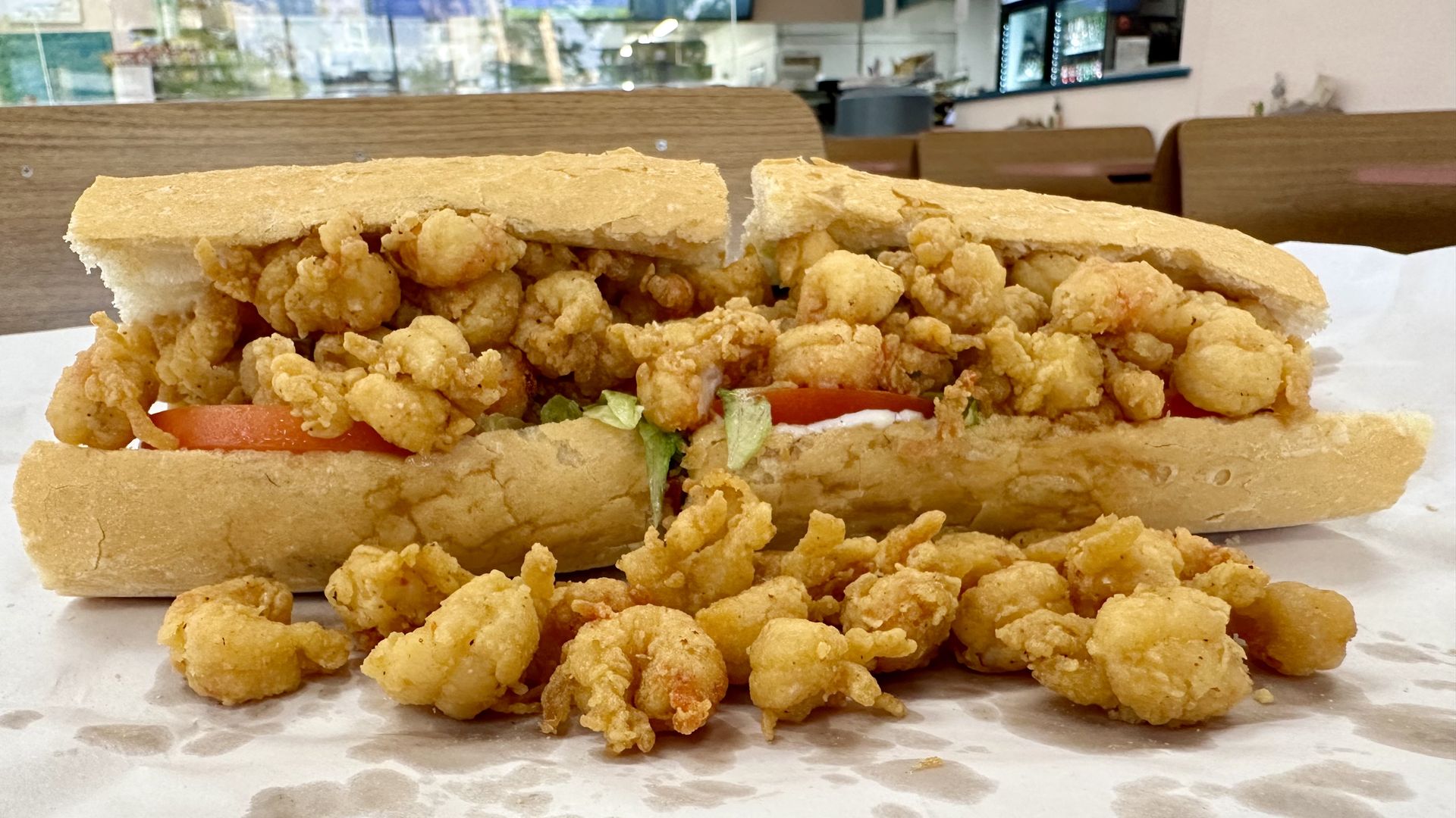 Photo shows fried crawfish tails falling out of an overstuffed poboy on a table
