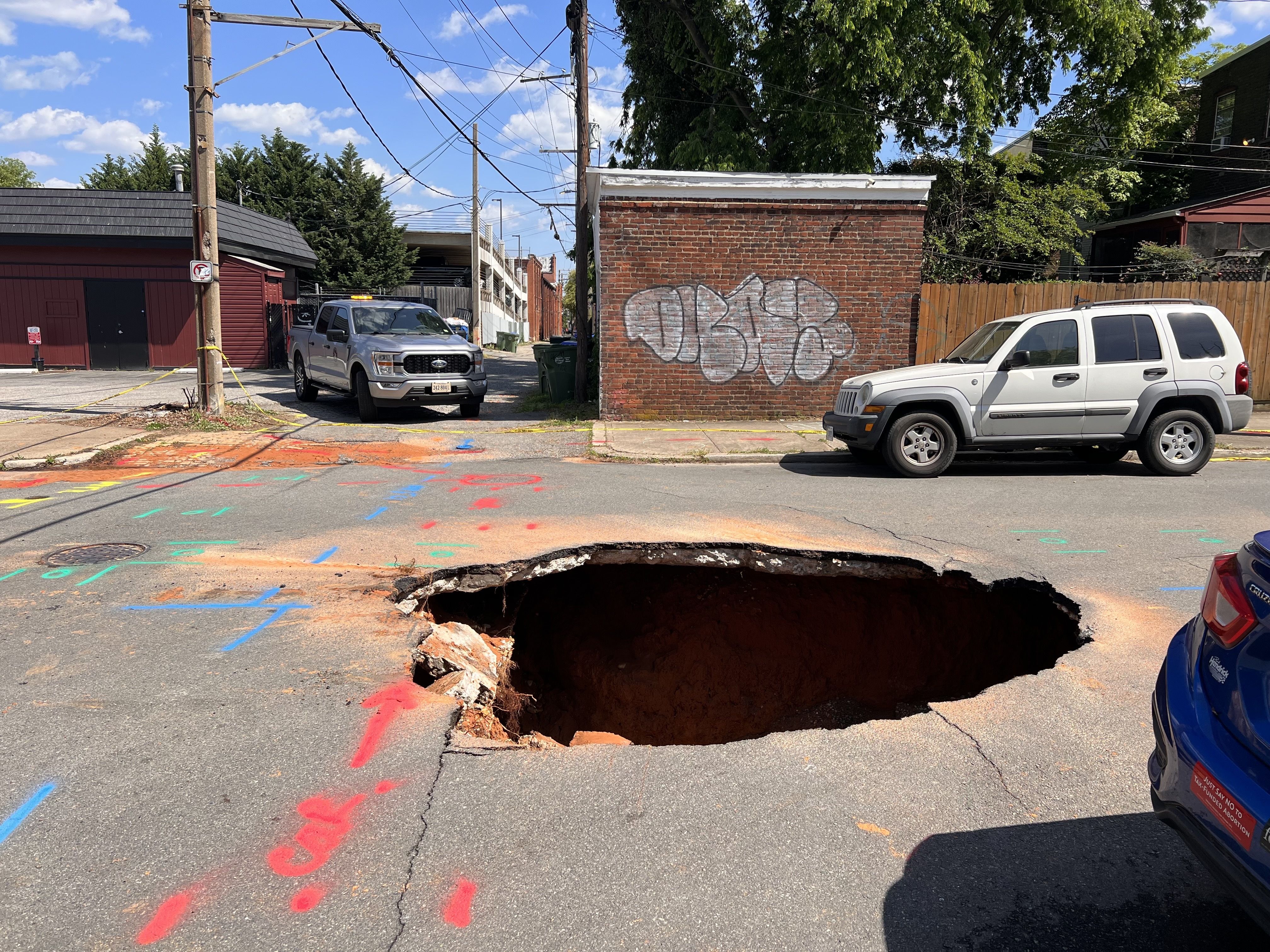 A massive sinkhole on a city street surrounded by cars.