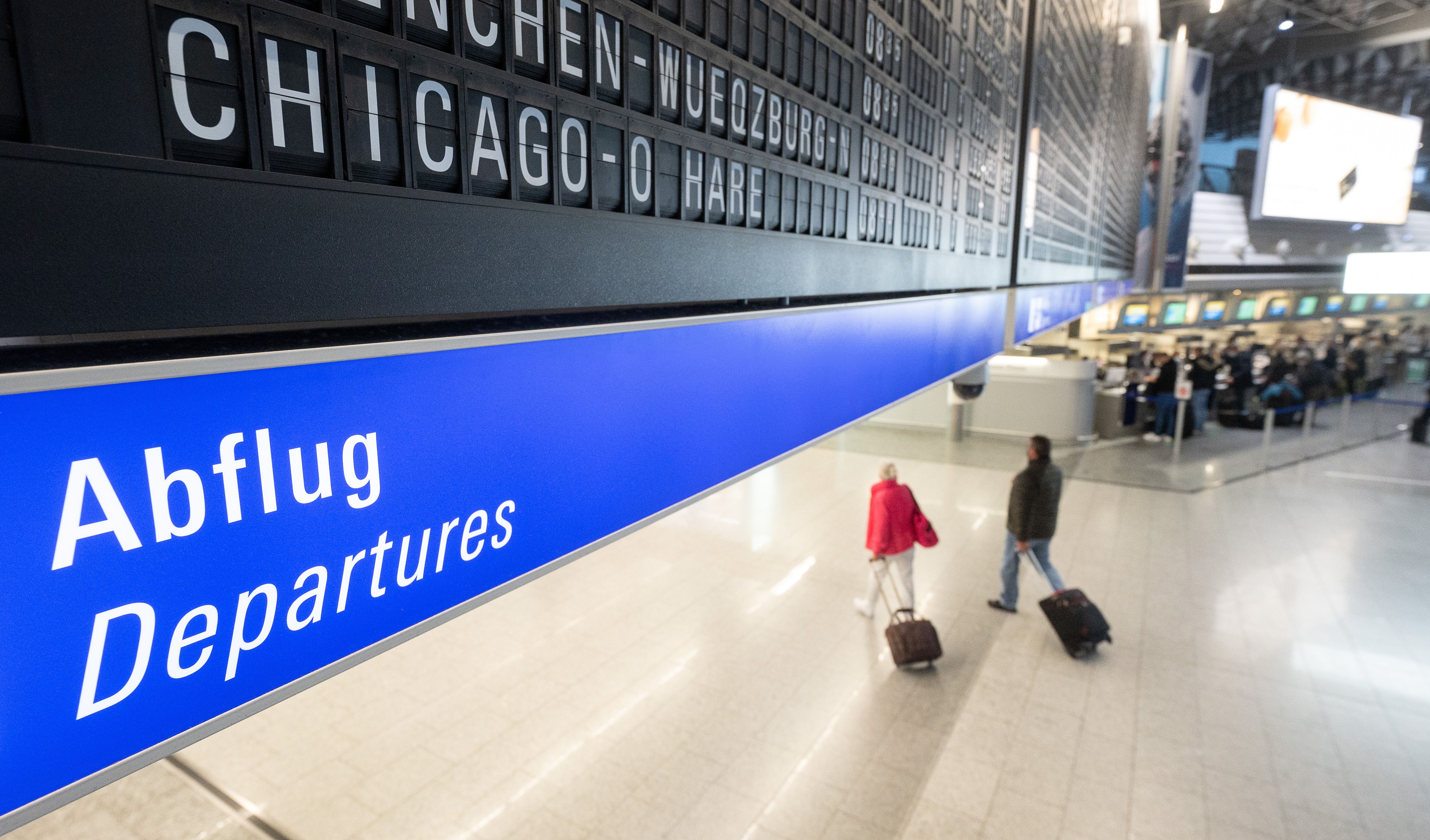  A flight to Chicago O'Hare in the U.S. is displayed on a board at Frankfurt airport under which passengers with suitcases walk along. 