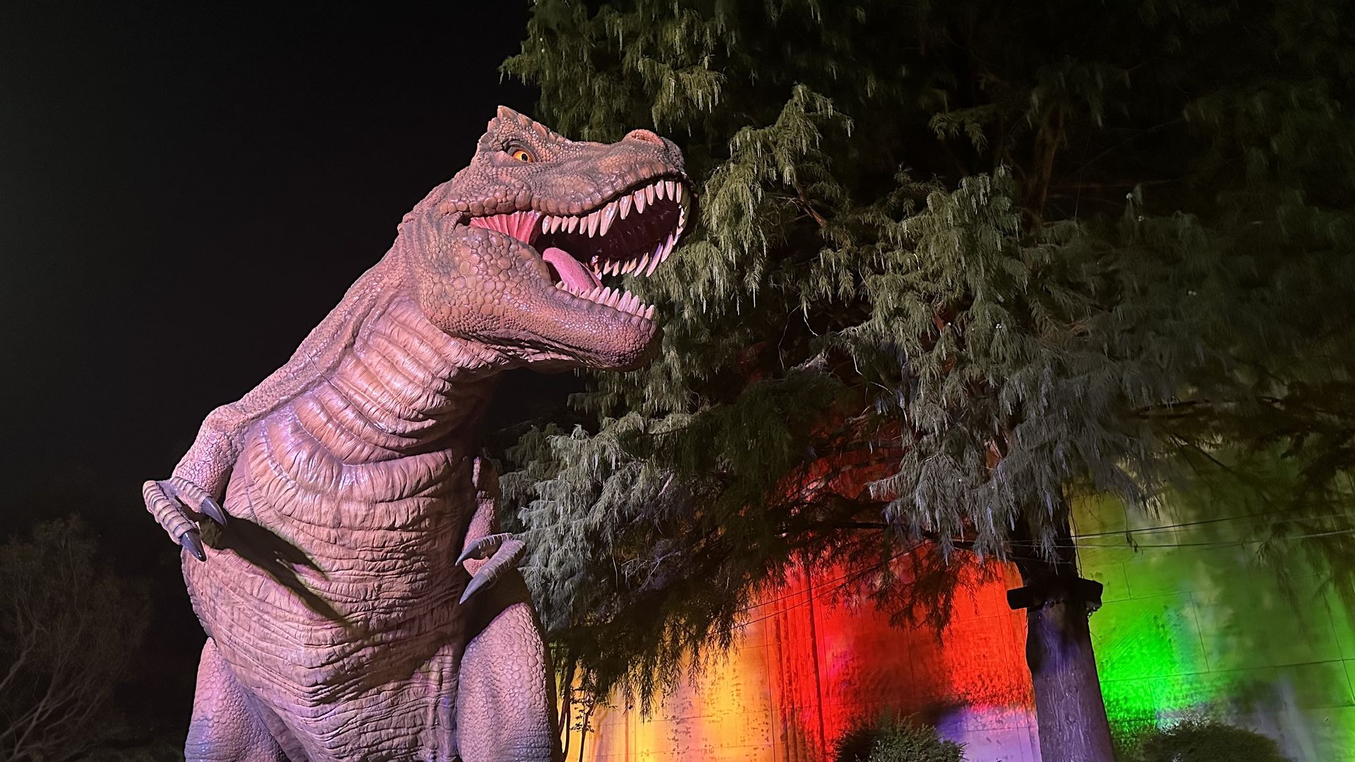 A fake dinosaur stands in the night with neon lights behind him