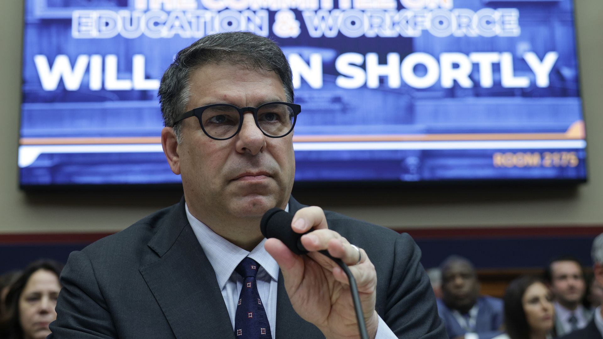 DePaul president Robert Manuel adjust a microphone.