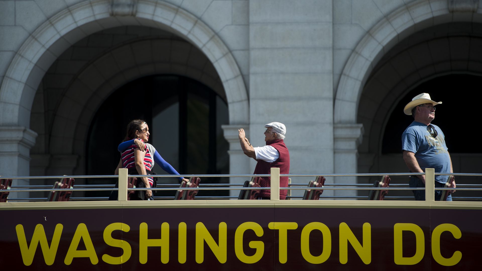 People on top of a double decker bus take a picture with the Union Station in the background