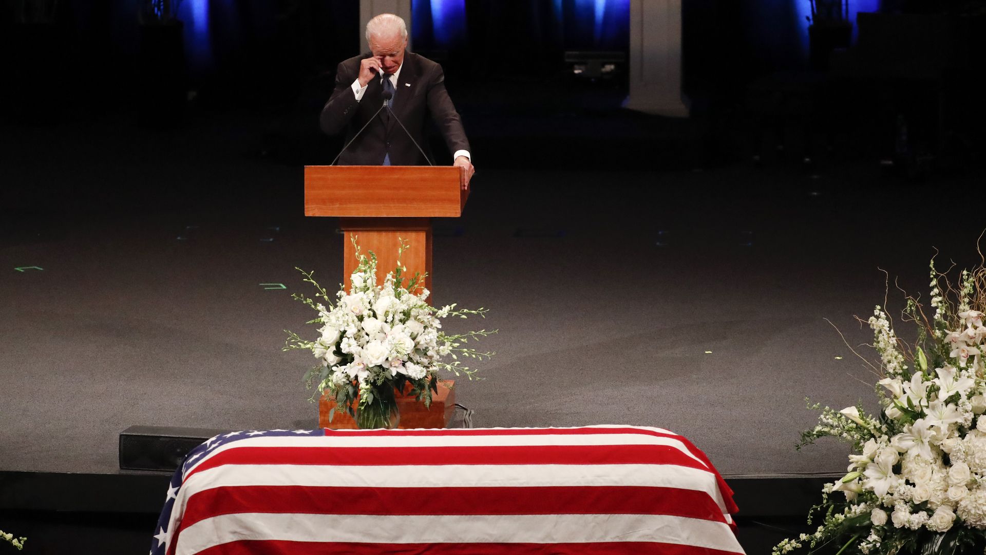 Joe Biden touches his face while crying standing at podium before McCain's casket covered in American flag