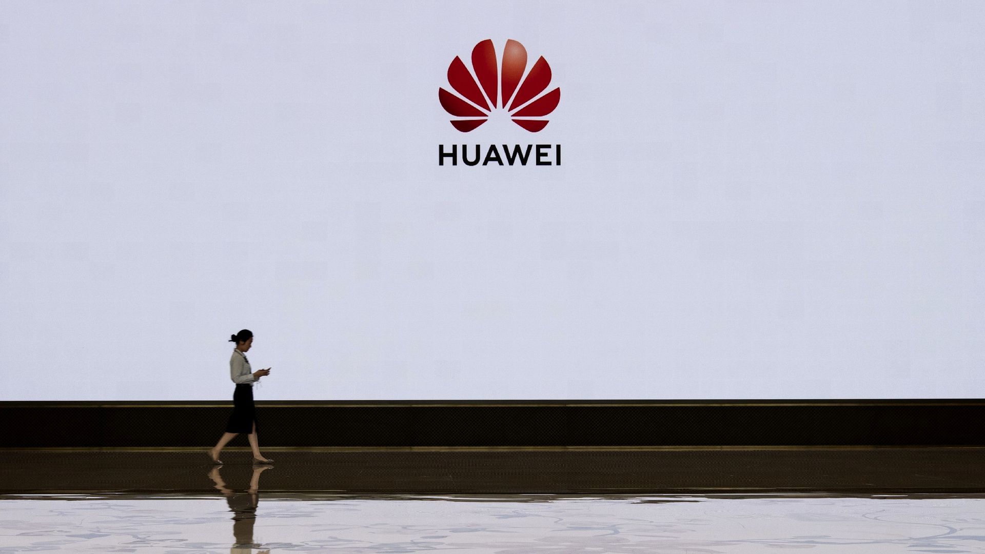 In this image, a woman walks by a large white wall that also includes the Huawei logo.