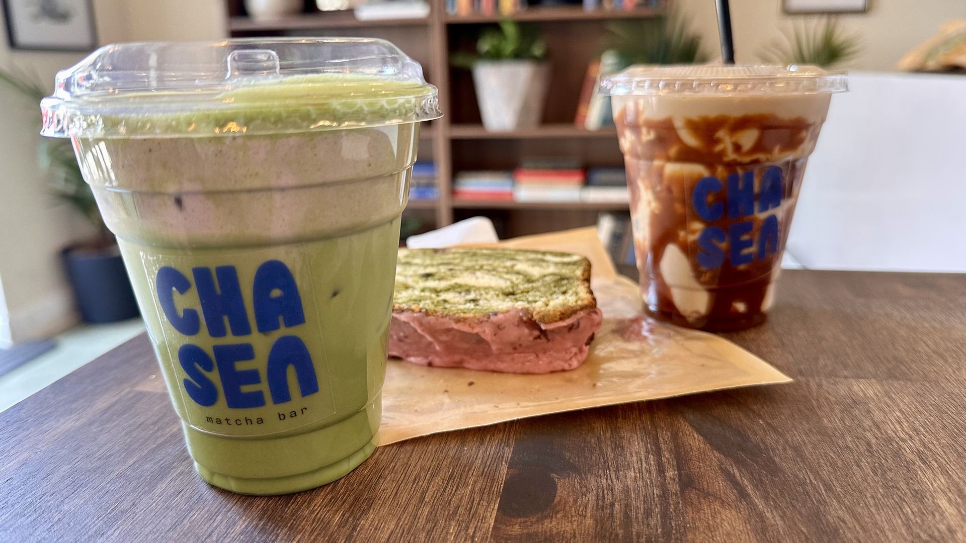 A photo of an iced matcha drink in front of a matcha loaf in front of another caramel iced drink 