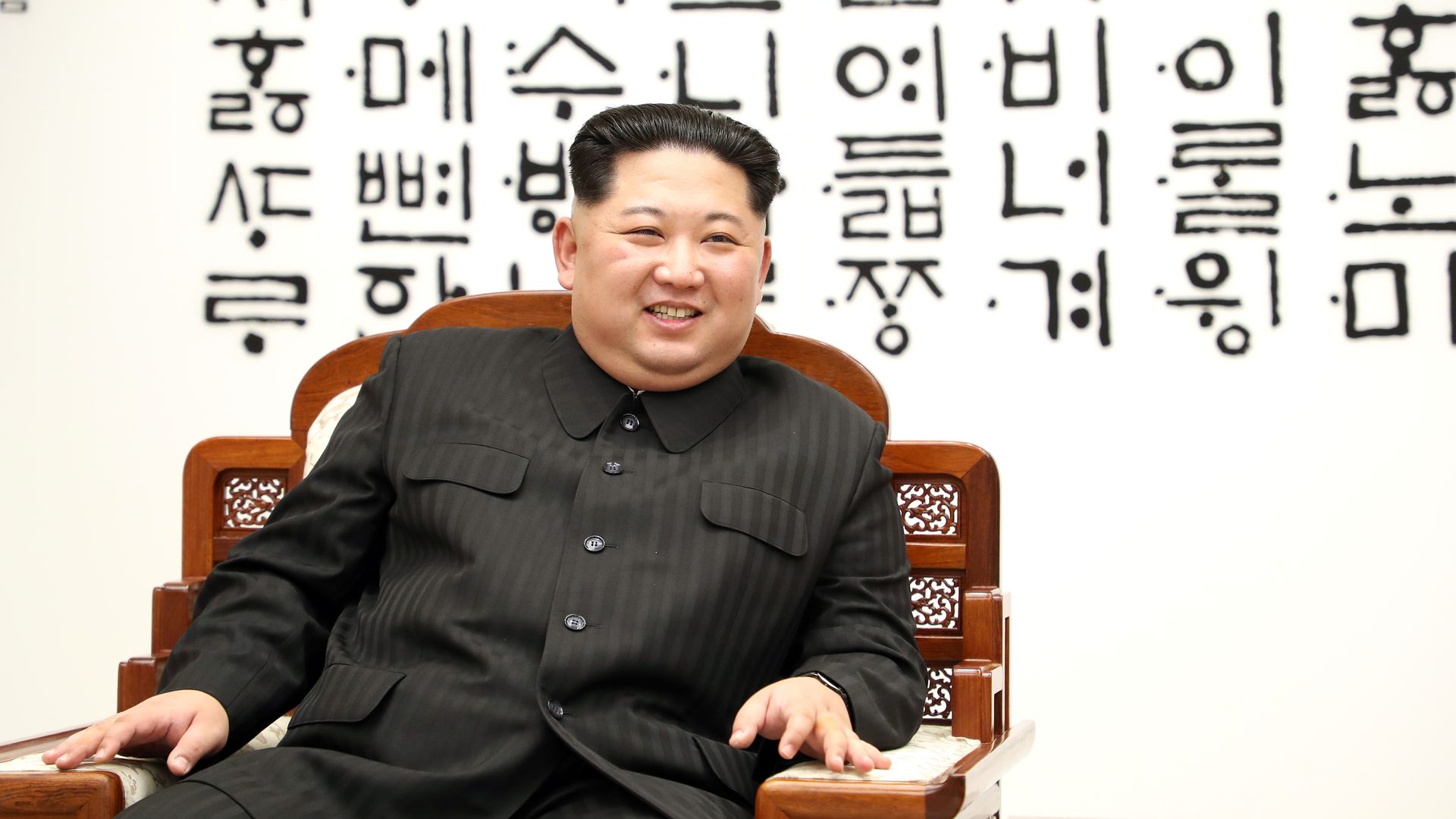Kim Jong-un sits in chair smiling.