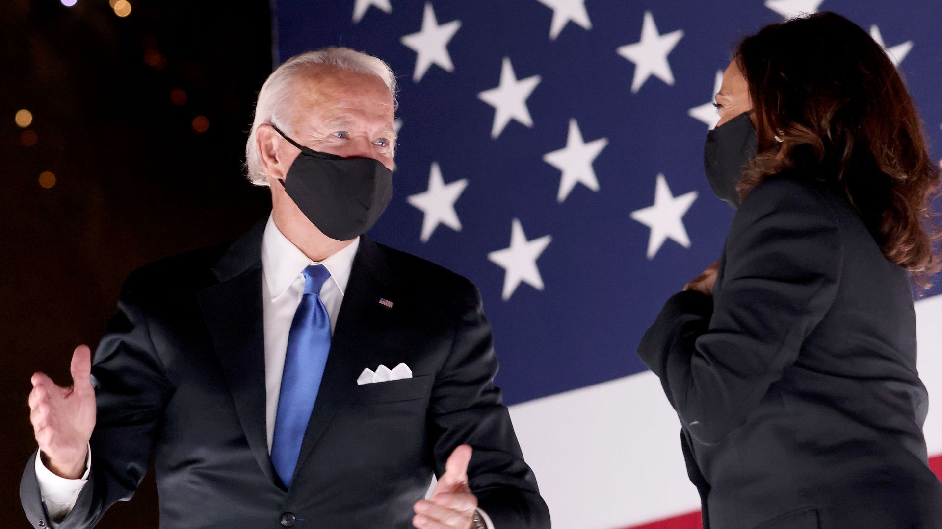 Biden and Harris stand together on stage in front of an American flag, wearing face masks
