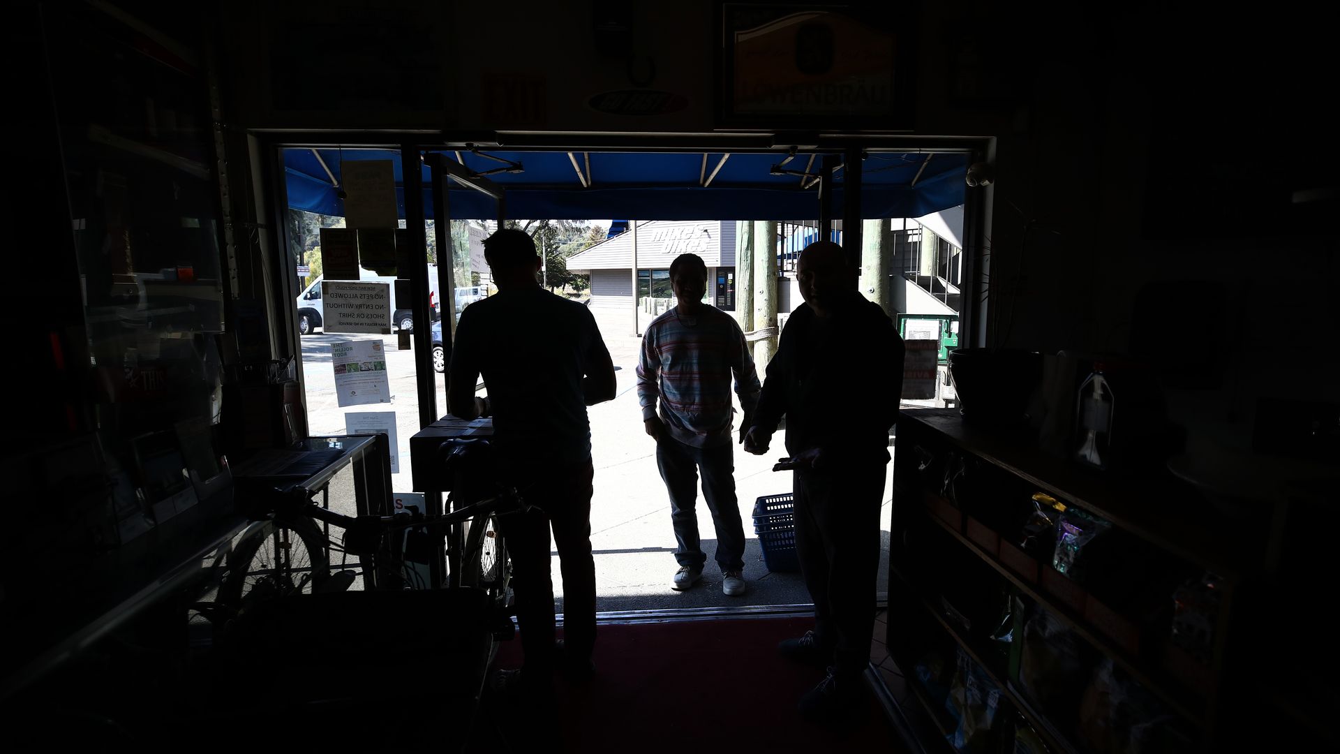 In this image, three silhouetted figures stand in front of an open and brightly lit garage door