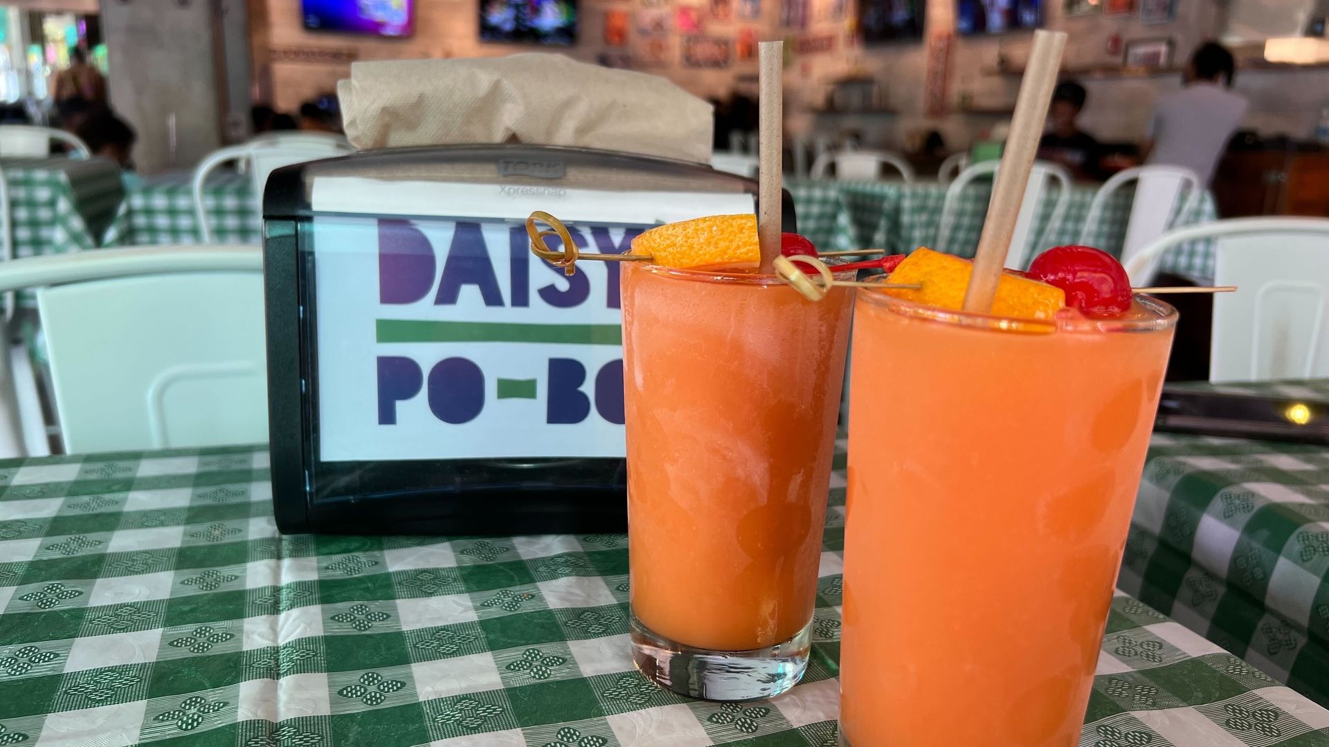 Napkin dispenser with 2 frozen, orange drinks topped with fruit and a brown straw.