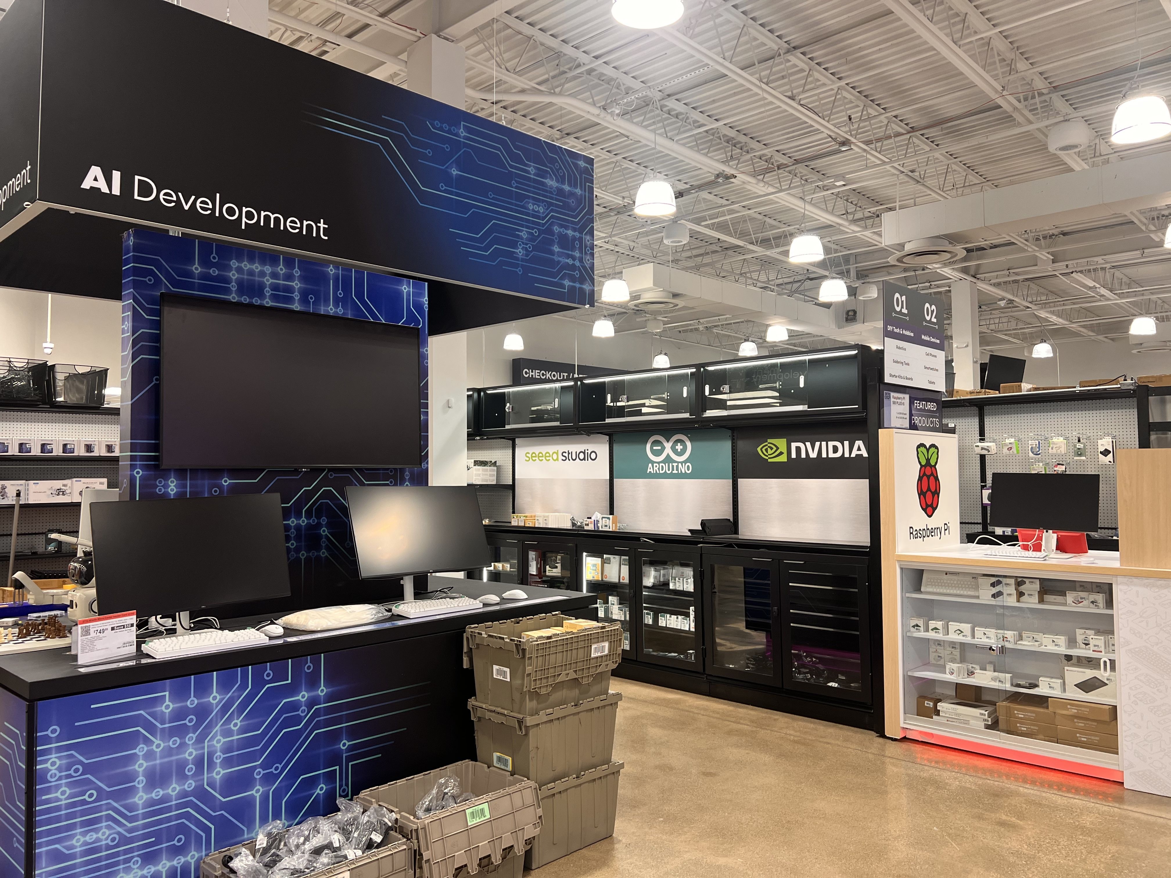 Inside a tech store, a large black and blue display reads "AI Development" with circuit graphics. Shelves, a checkout area, and NVIDIA and Raspberry Pi signs are visible.