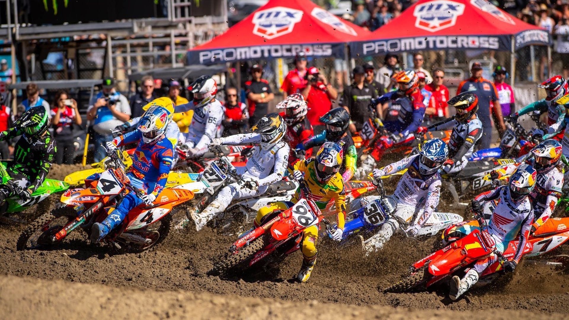 A wave of motocross racers make a hard right turn on a dirt track