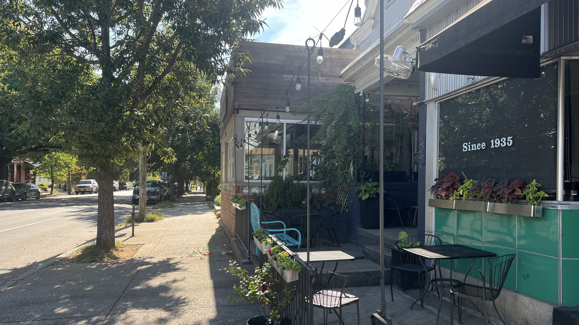 A sidewalk with trees and a bar on the right hand corner that has the words "since 1935" on the windows