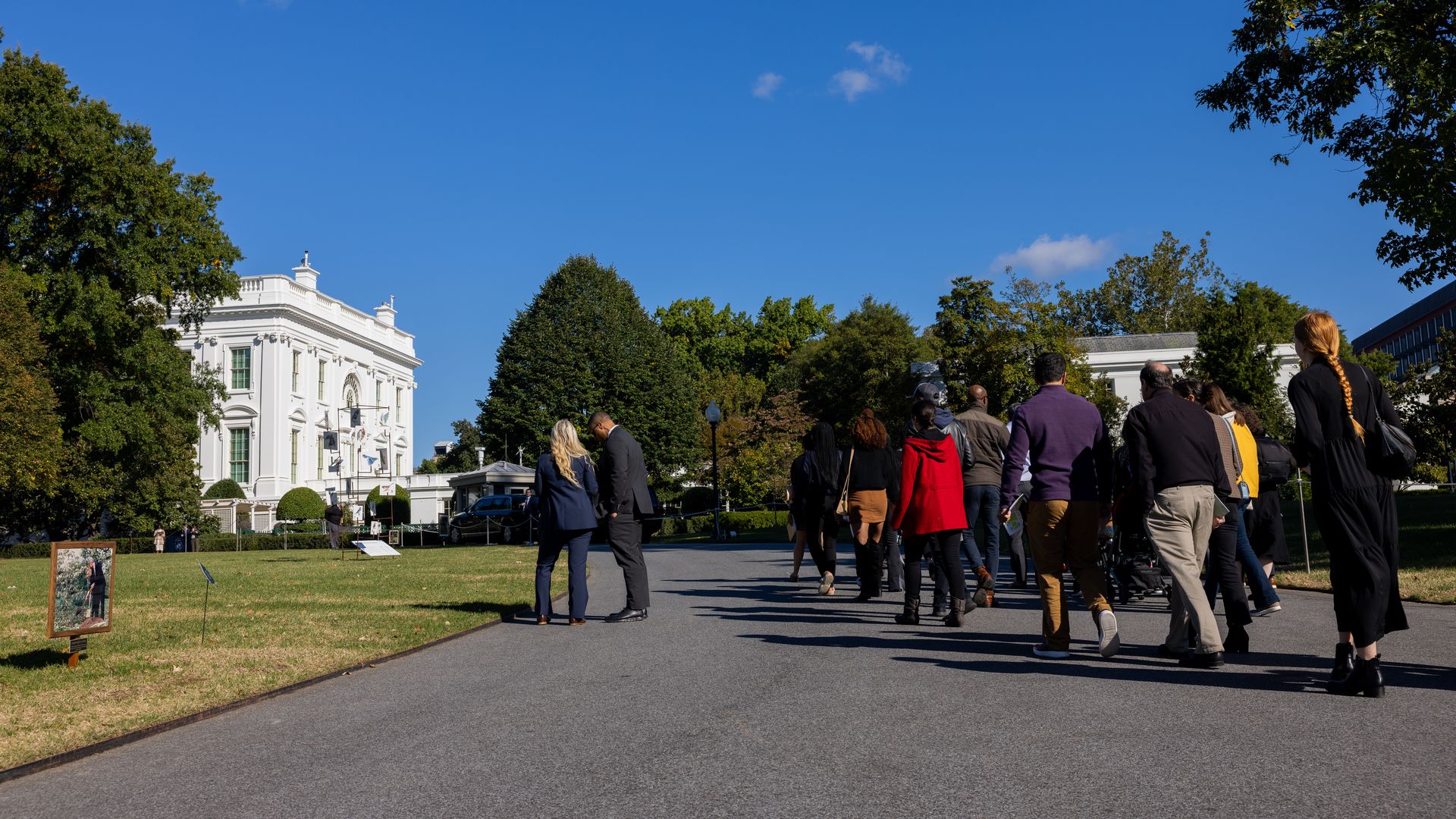 About a dozen people wearing winter coats walk towards the White House.