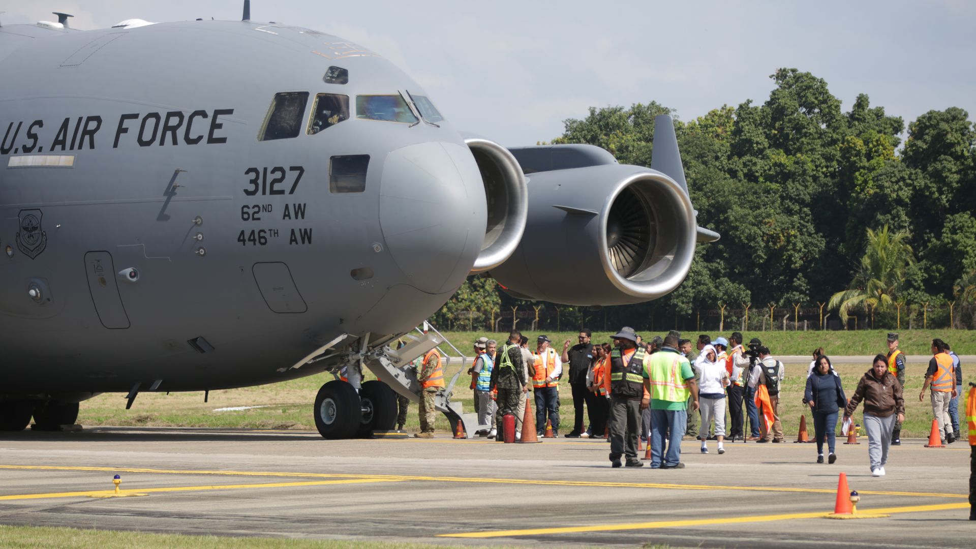 A large U.S. military plane with several immigrants on a tarmac.