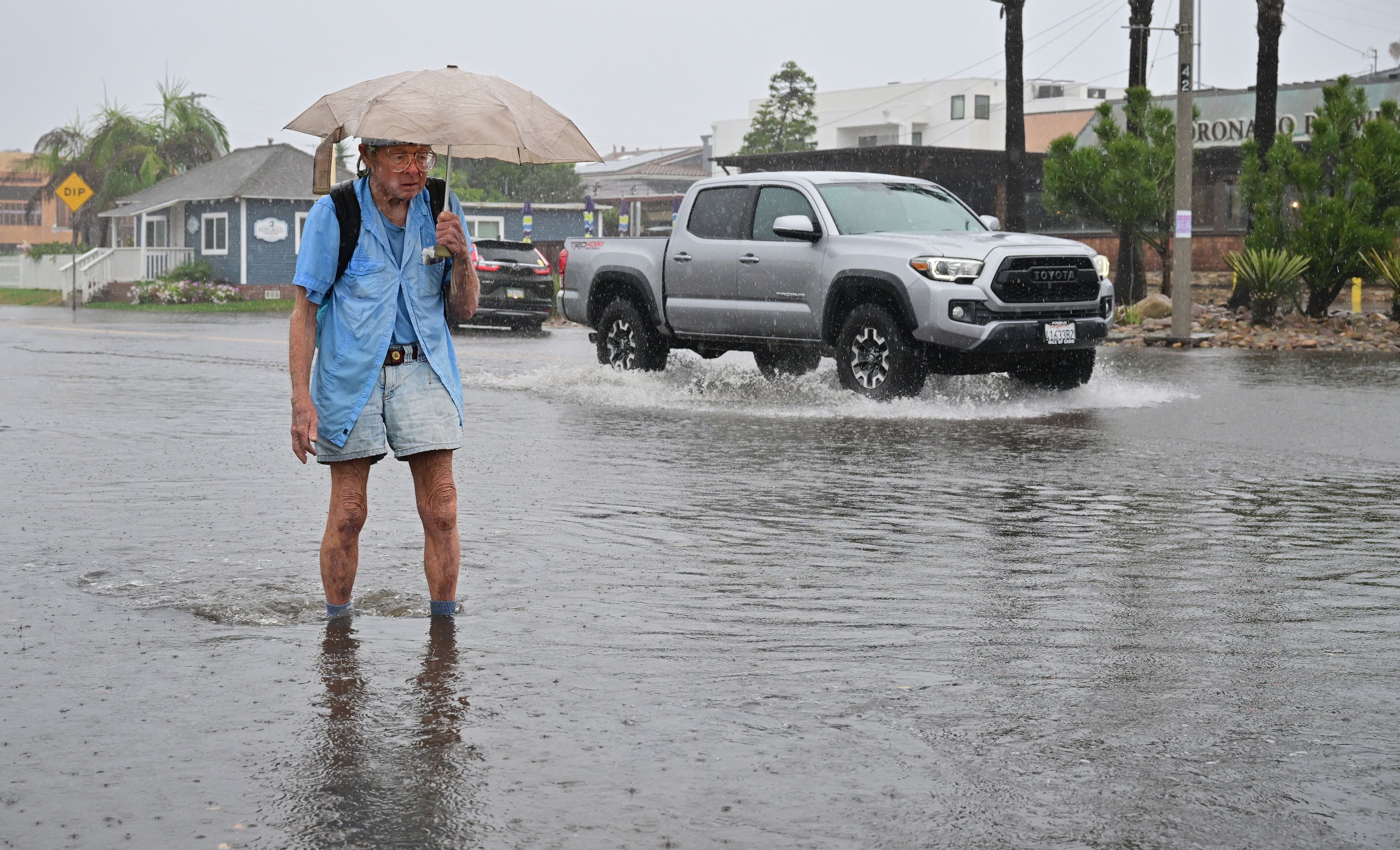 Patrick Brown holds his umbrella as he makes his way across a flooded intersection in Imperial Beach, California on August 20, 2023. Hurricane Hilary weakened to a tropical storm on August 20, 2023, as it barreled up Mexico's Pacific coast, but was still likely to bring life-threatening flooding to the typically arid southwestern United States, forecasters said. Authorities reported at least one fatality in northwestern Mexico, where Hilary lashed the Baja California Peninsula with heavy rain and strong winds