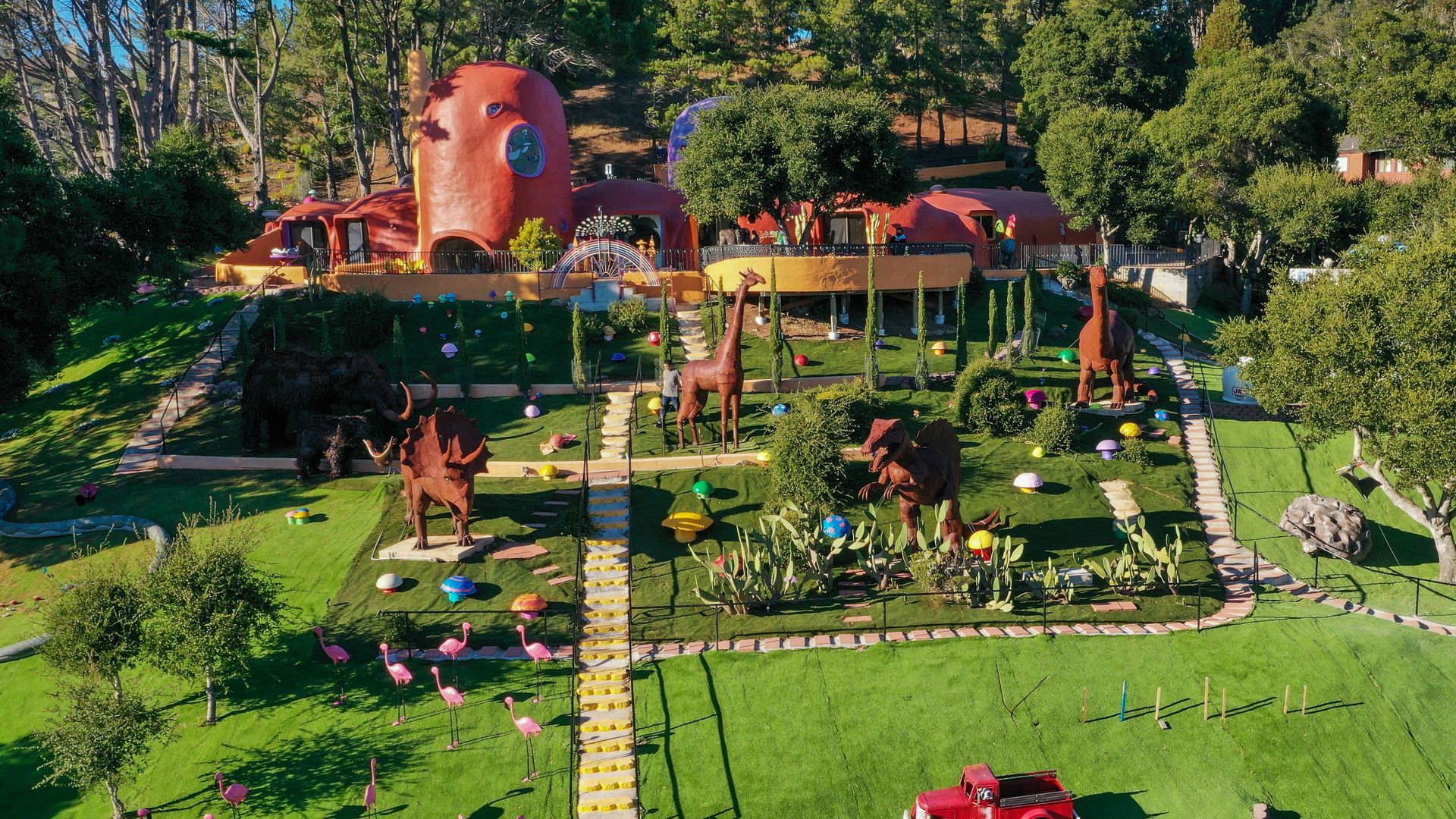Photo of a round orange and purple house with colorful animal sculptures and mushrooms dotting the lawn