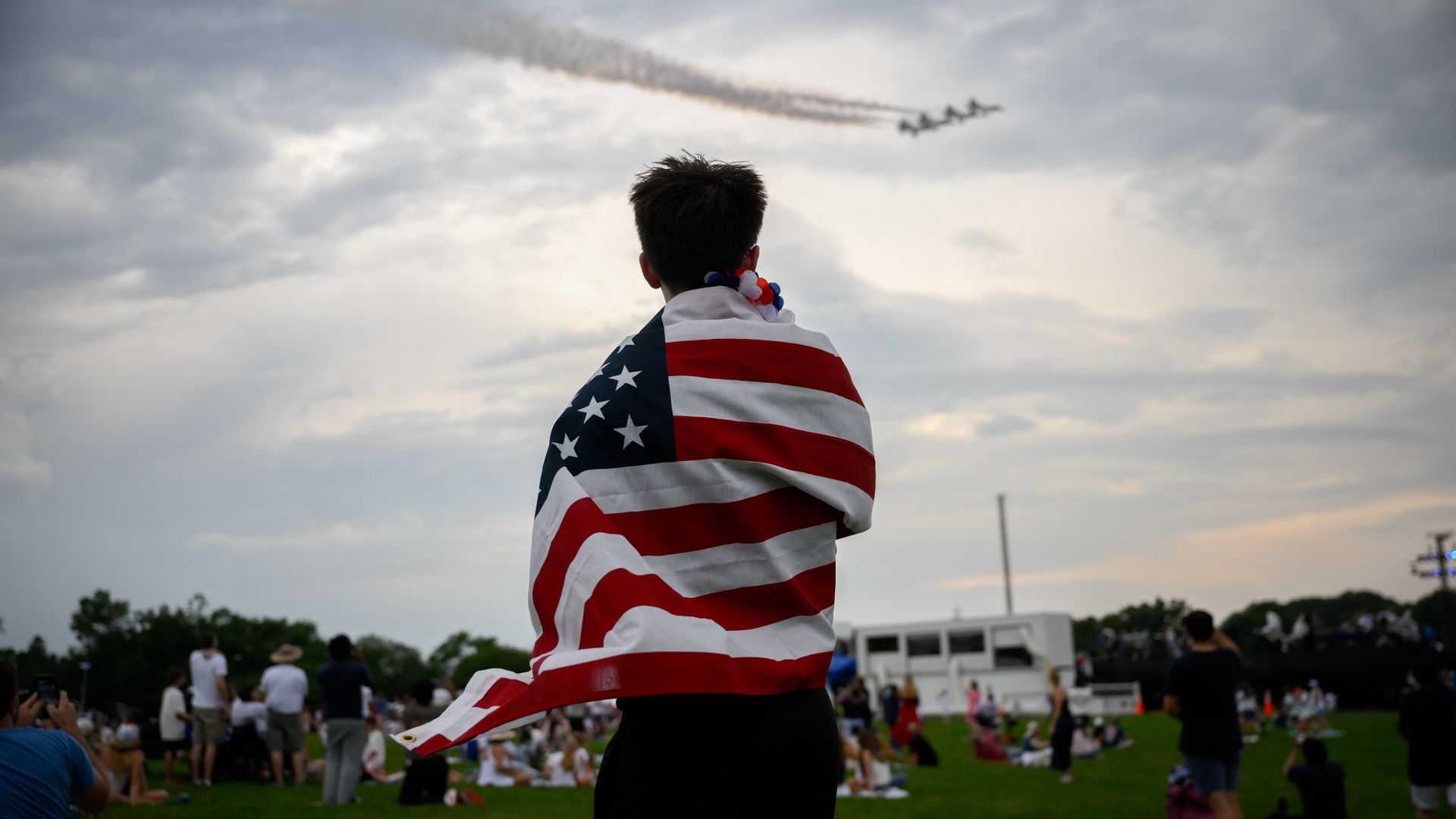 An attendee wrapped in a US flag watches a flyover near the Washington Monument during the "Salute to America" event on the National Mall