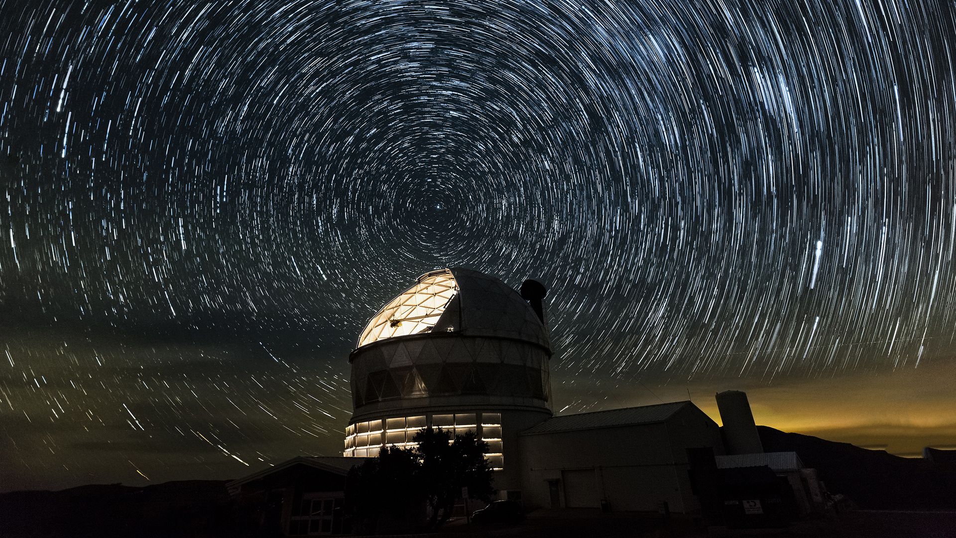 A telescope at the McDonald Observatory, with stars swirling overhead.