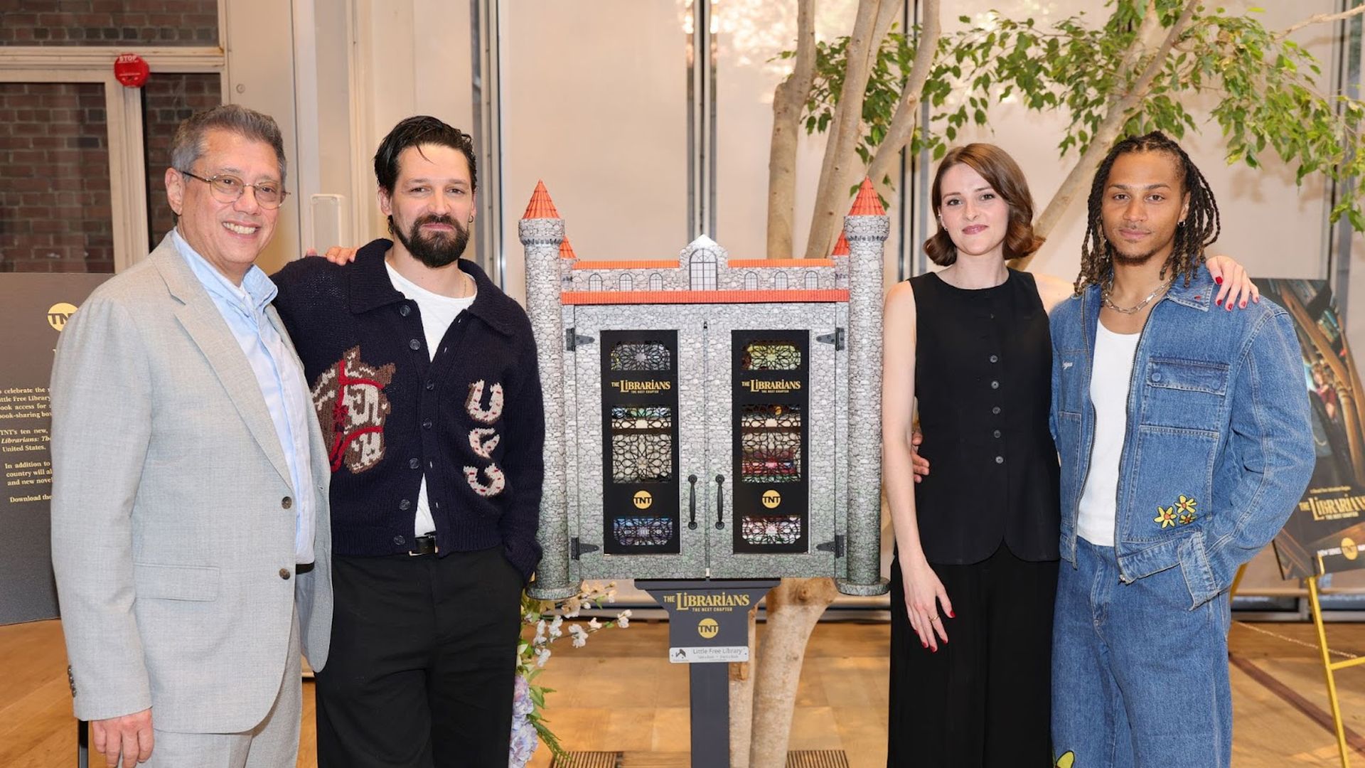 Dean Devlin, Callum McGowan, Olivia Morris and Bluey Robinson — cast members of TNT new series The Librarians: The Next Chapter, stand with a themed Little Free Library