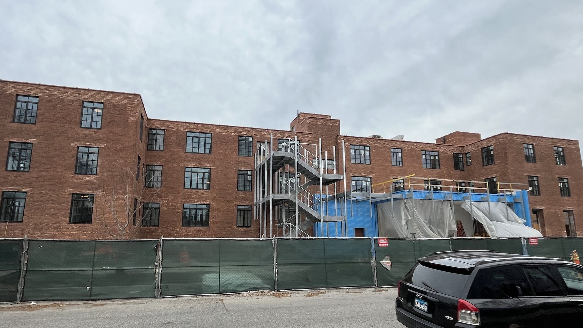 Brick building with green fence in front and tiered scaffolding in front.