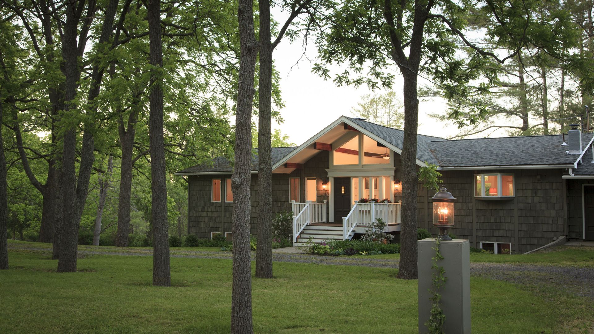a suburban home in a wooded area, lit up during early evening hours