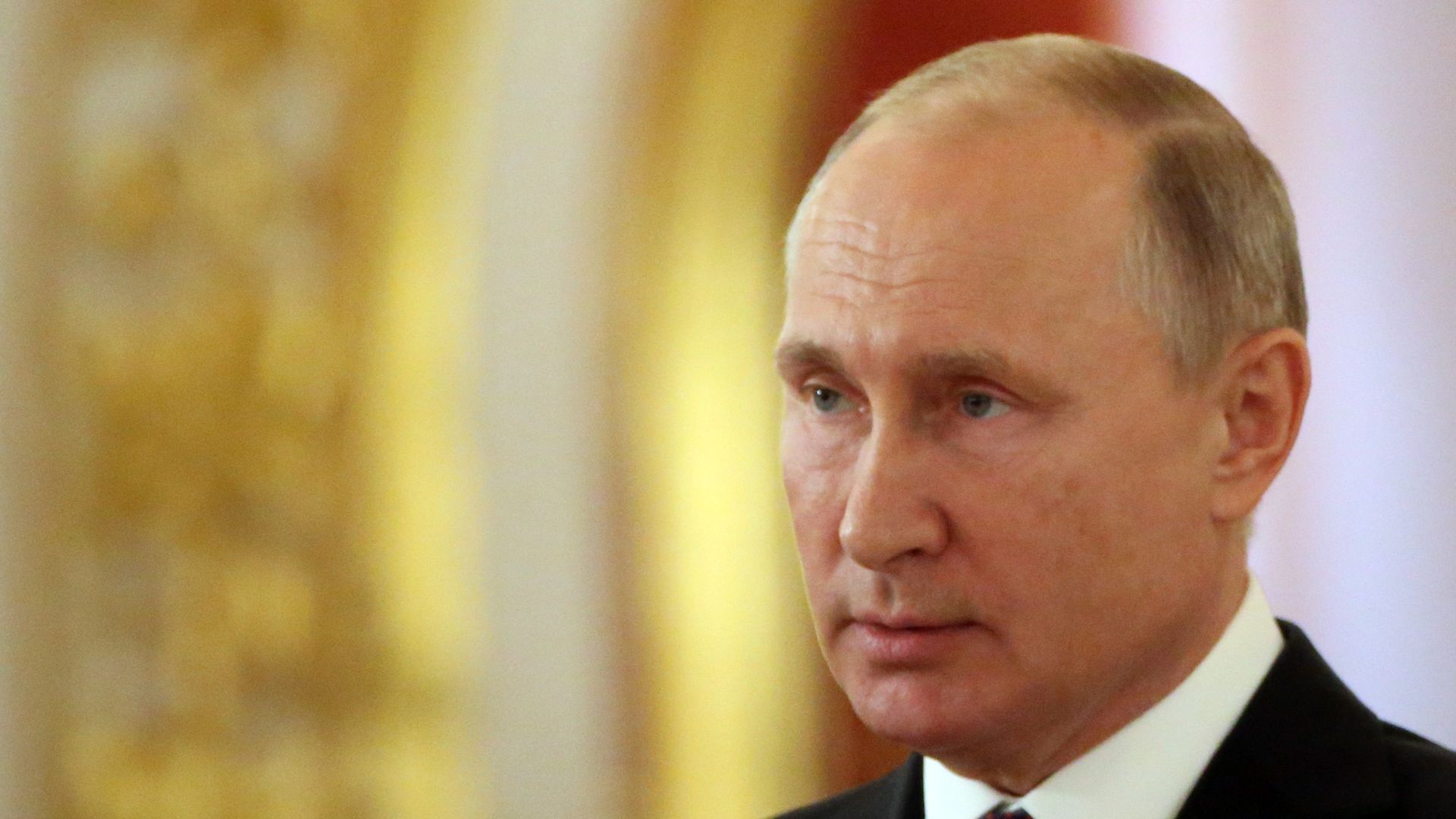 Vladimir Putin looks stoic before gold background.