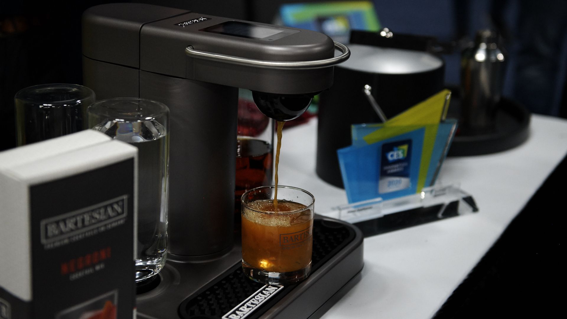 A Bartesian cocktail maker, which is a small kitchen appliance in black that uses pods to make cocktails, sits on a countertop.