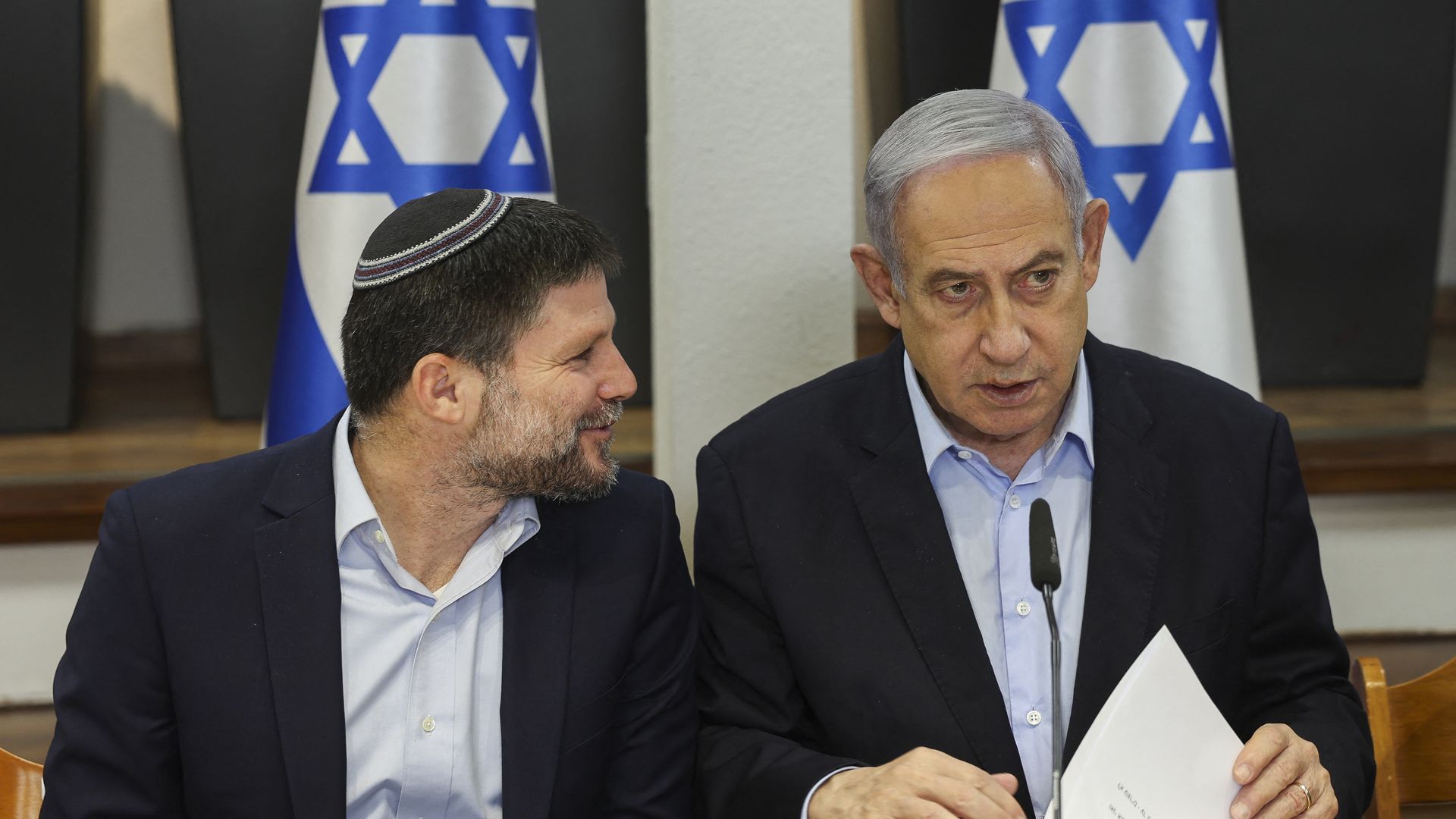Two men in front of Israeli flags at a conference table