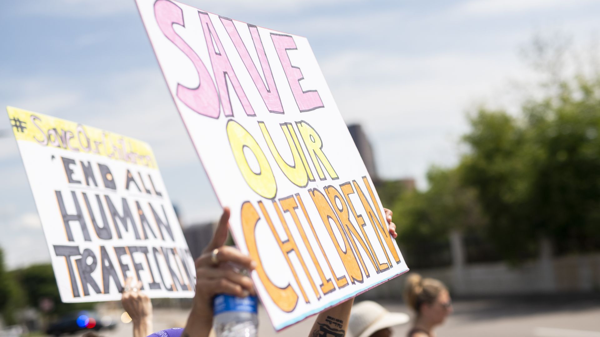Signs at a protest read "Save our children" and "End all human trafficking." 
