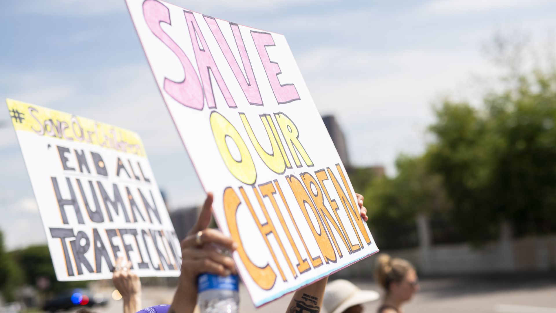 Signs at a protest read "Save our children" and "End all human trafficking."