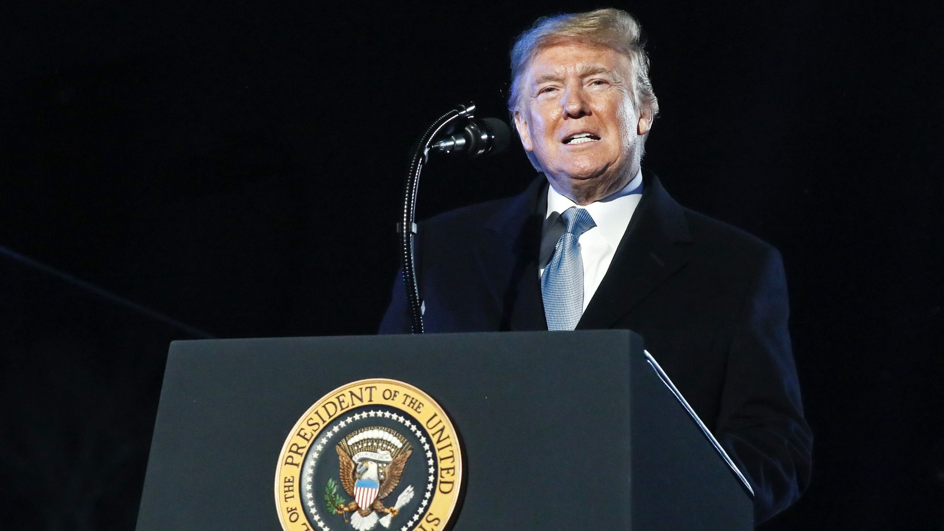 In this image, Trump stands in front of a podium with the seal of the President on it