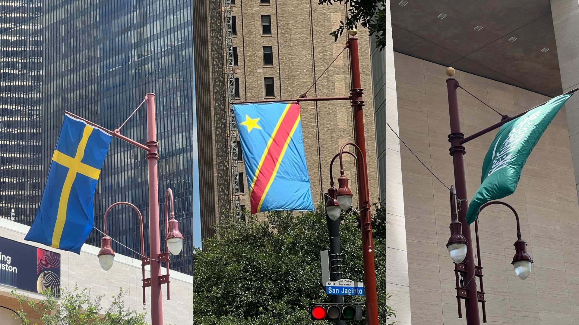 Three flags on red lamp posts along a city street: left blue with a yellow Nordic cross, middle blue with a diagonal red stripe and yellow border with a star, right green with a white emblem; glass and brick skyscrapers behind.