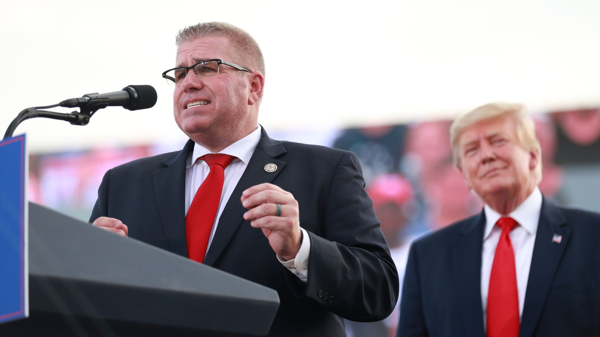 Photo of a man behind a podium speaking at a rally.